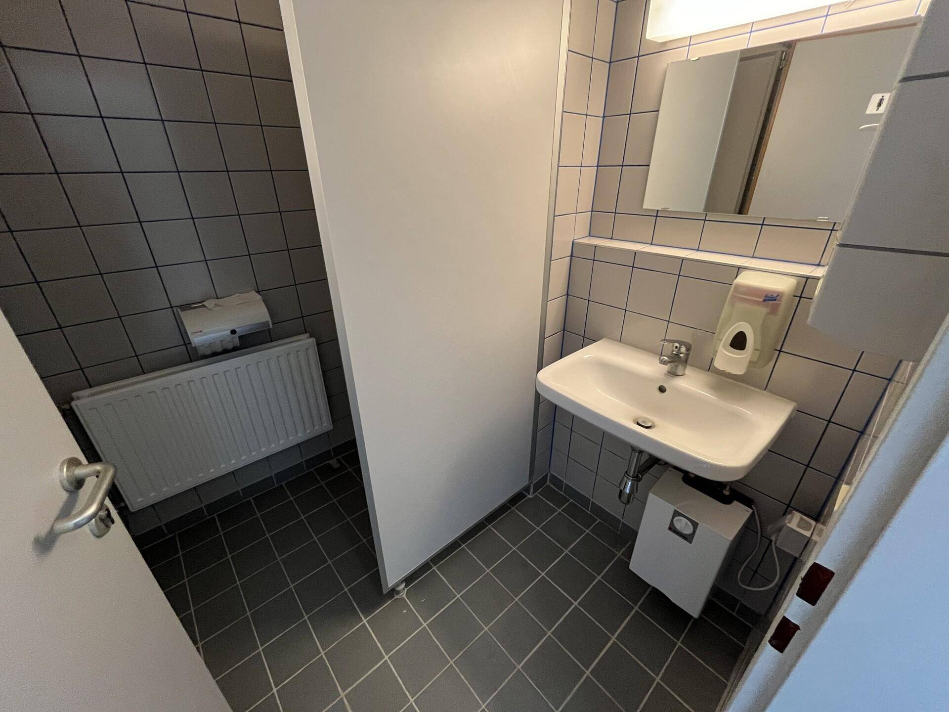 Saubere Toilette mit Waschbecken, Spiegel und grauen Wand- und Bodenfliesen in gutem Zustand.