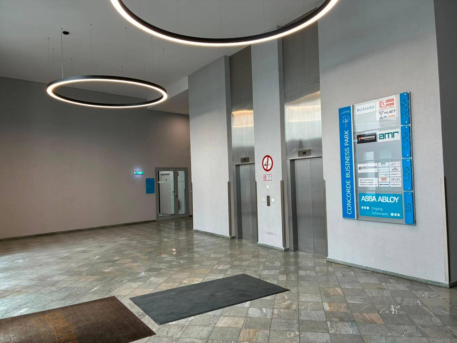 Moderne Lobby mit Aufzügen, Marmorboden und stilvollen runden Deckenleuchten.