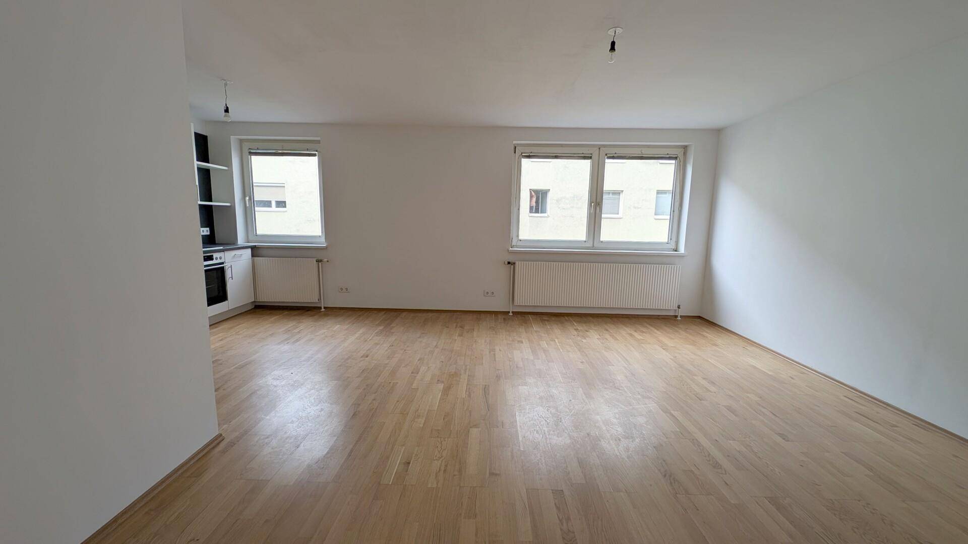 Geräumiges Wohnzimmer mit hellem Parkettboden und zwei großen Fenstern.