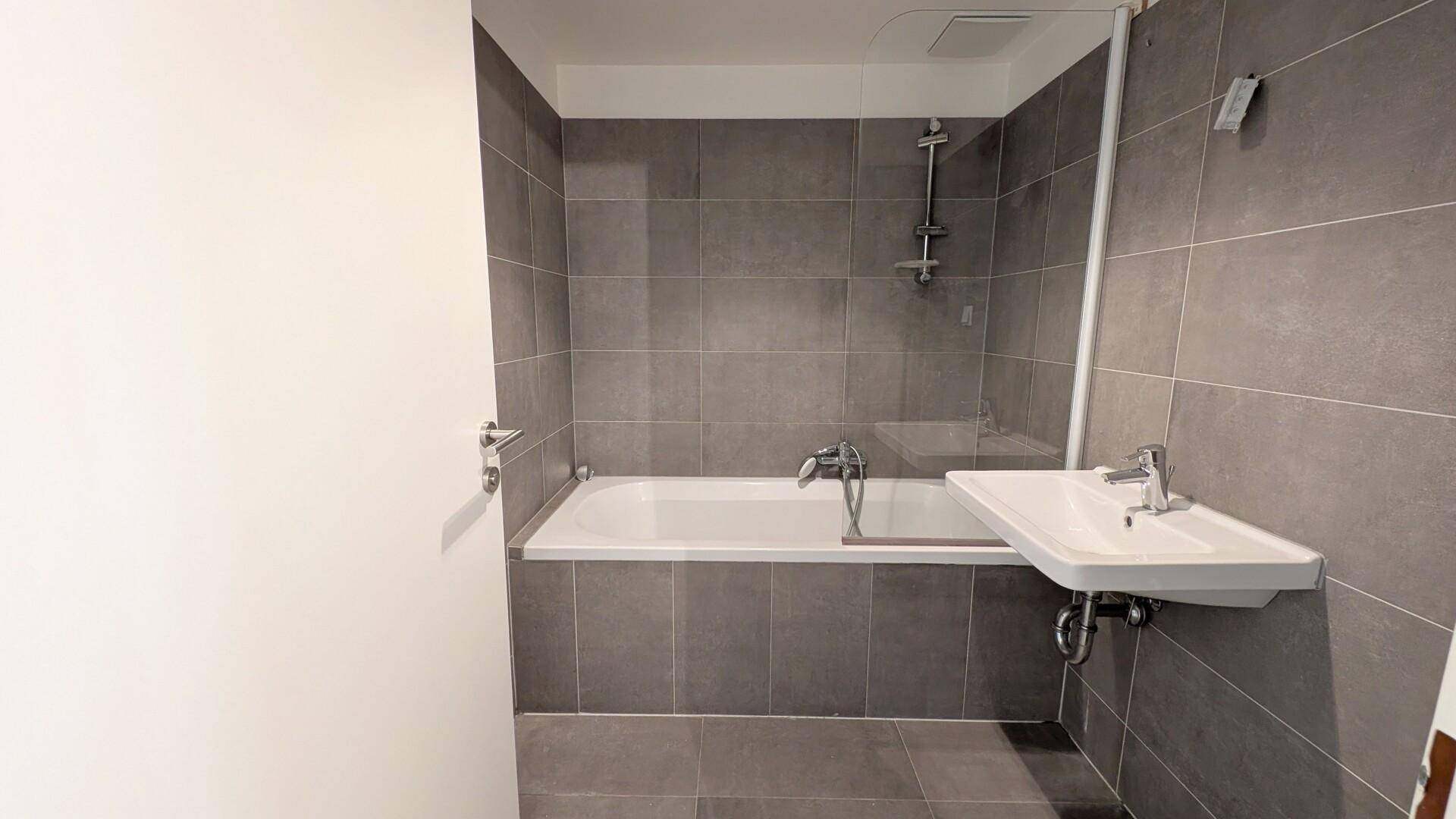 Modernes Badezimmer mit grauen Fliesen, Badewanne und Waschbecken.