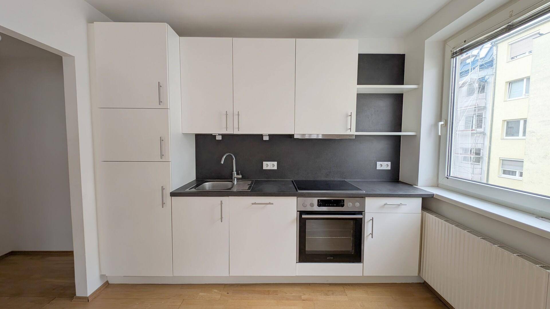 Moderne Einbauküche in Weiß mit dunkler Arbeitsplatte und Fensterblick.