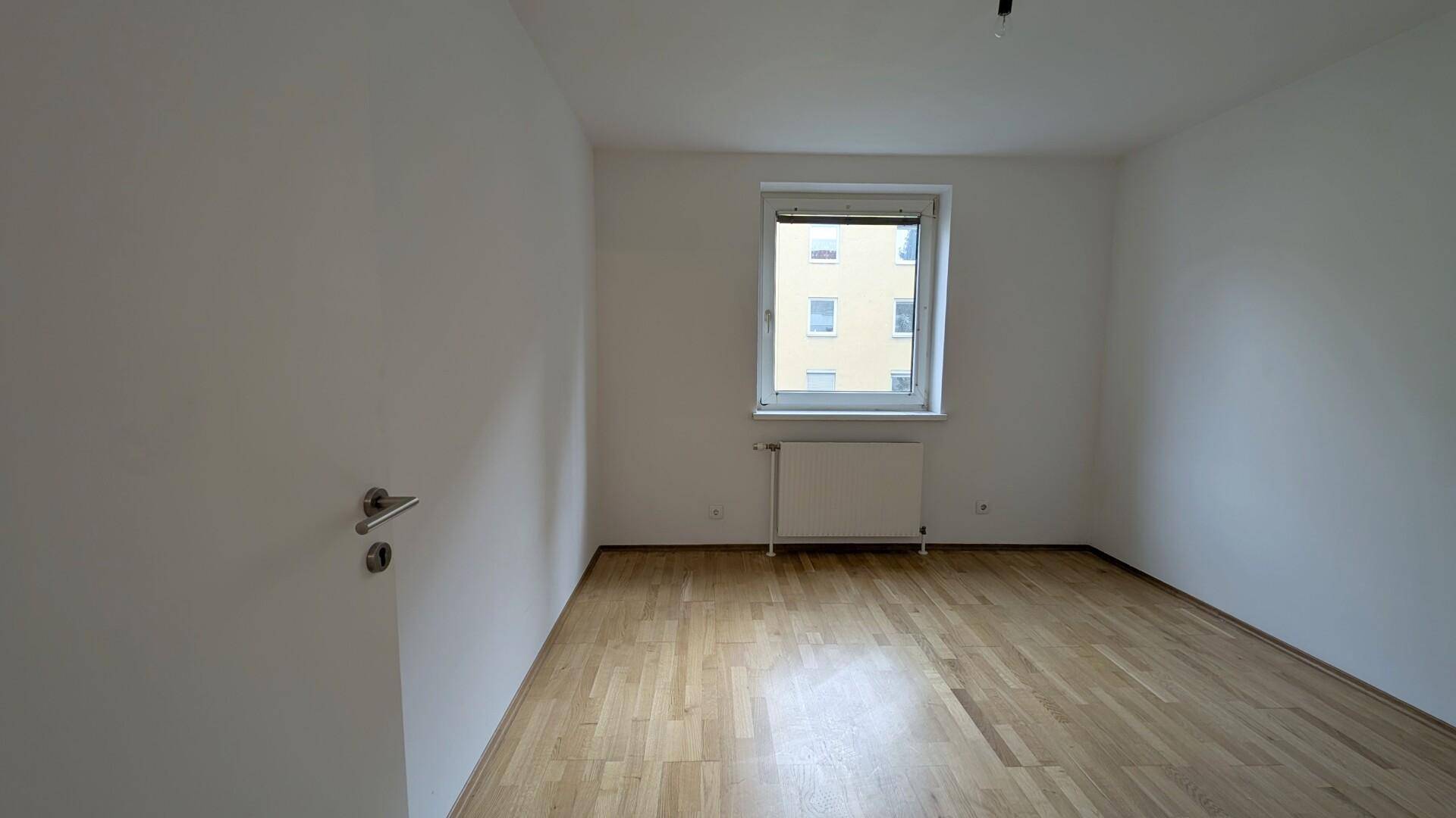 Helles Schlafzimmer mit Parkettboden und einem Fenster, bereit zur individuellen Gestaltung.
