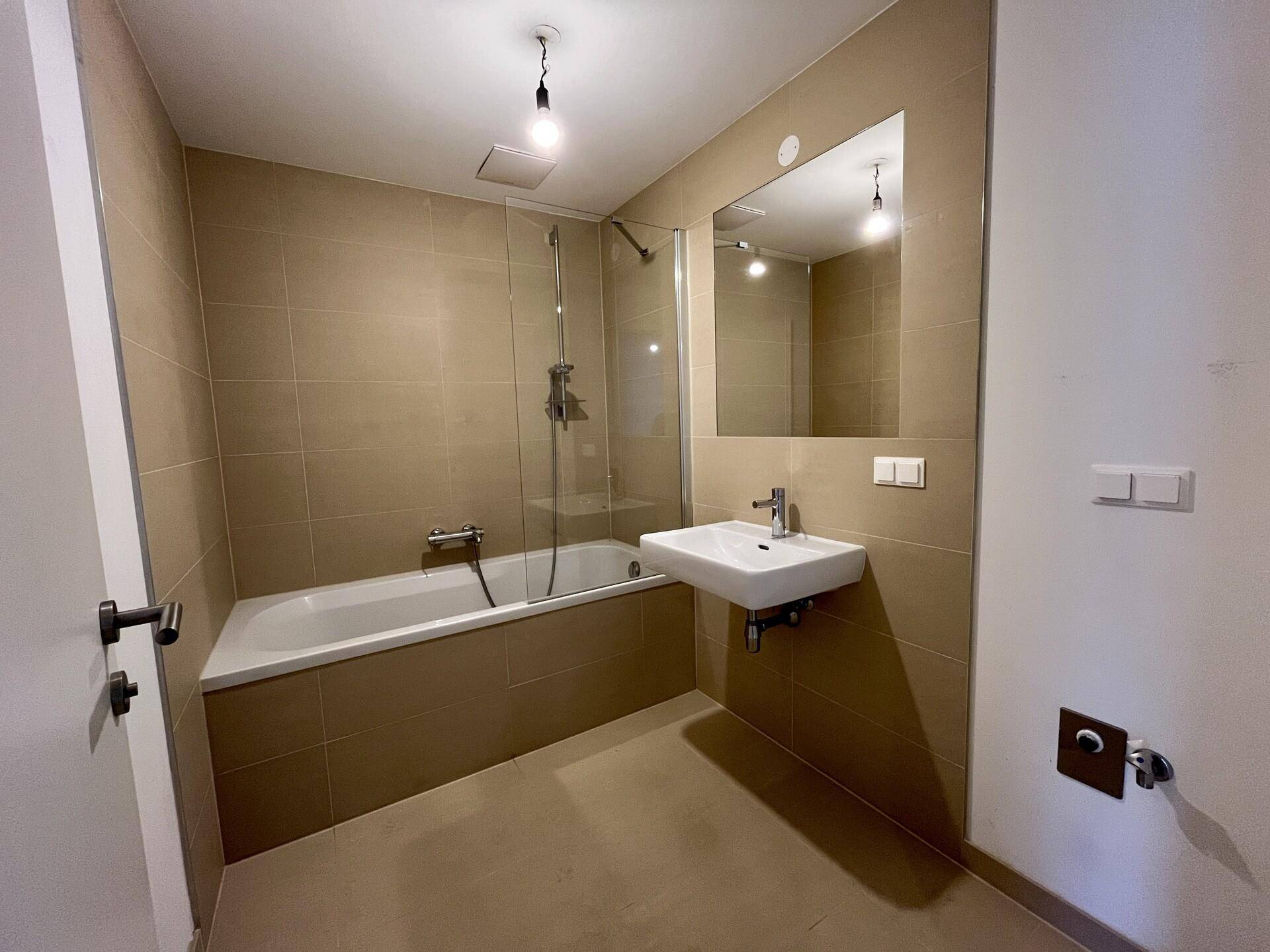 Modernes Badezimmer mit beigefarbenen Fliesen, Badewanne mit Duschfunktion und Einzelwaschbecken.