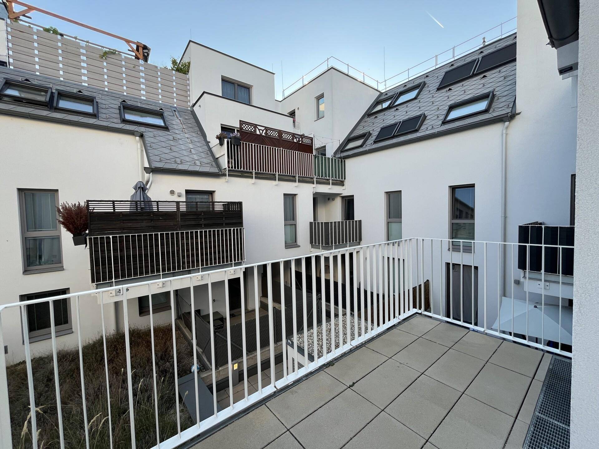 Balkon mit Fliesenboden und Blick auf den begrünten Innenhof der Wohnanlage.
