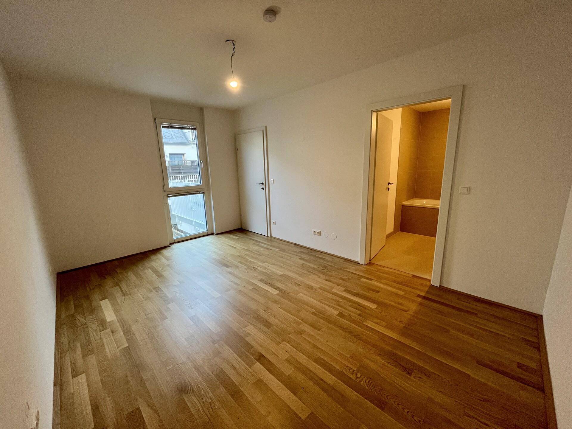 Geräumiges Schlafzimmer mit Holzparkettboden und direktem Zugang zu einem Badezimmer.