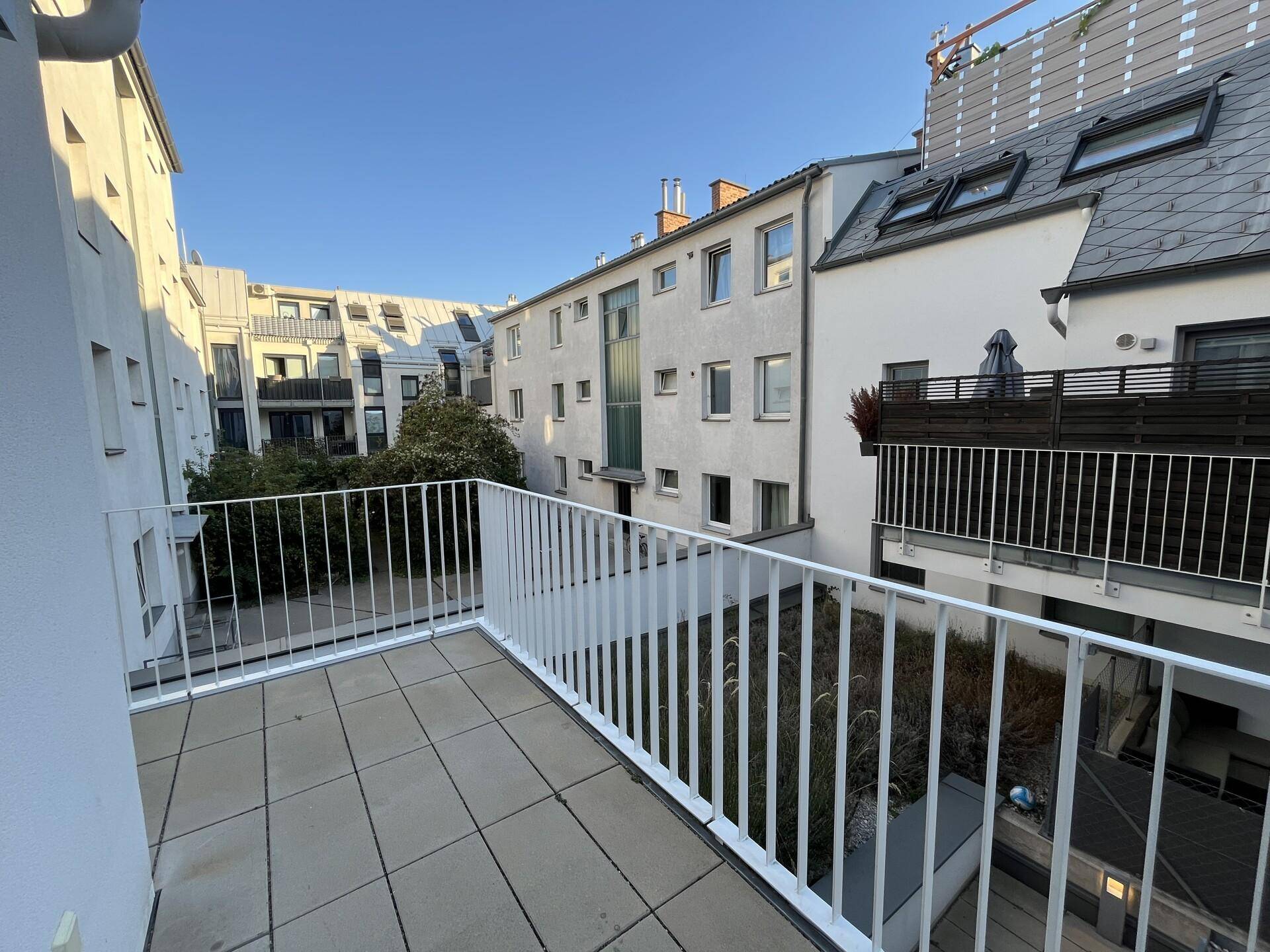 Heller Balkon mit Fliesenboden und Blick auf den ruhigen Innenhof der Wohnanlage.