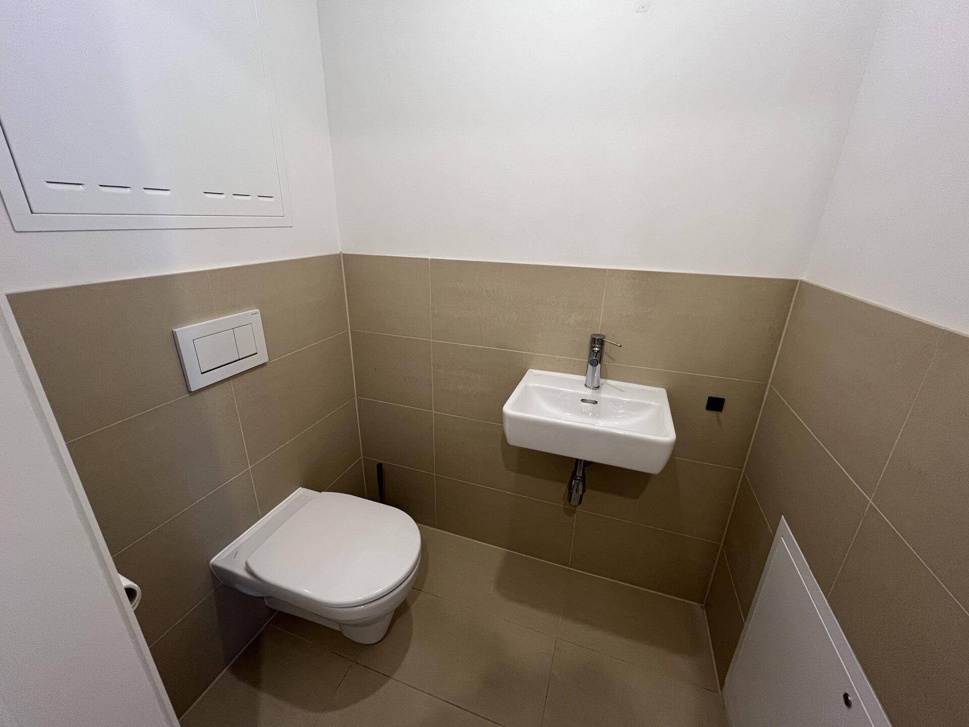 Modernes Gäste-WC mit beigefarbenen Fliesen, wandhängendem WC und kleinem Waschbecken.