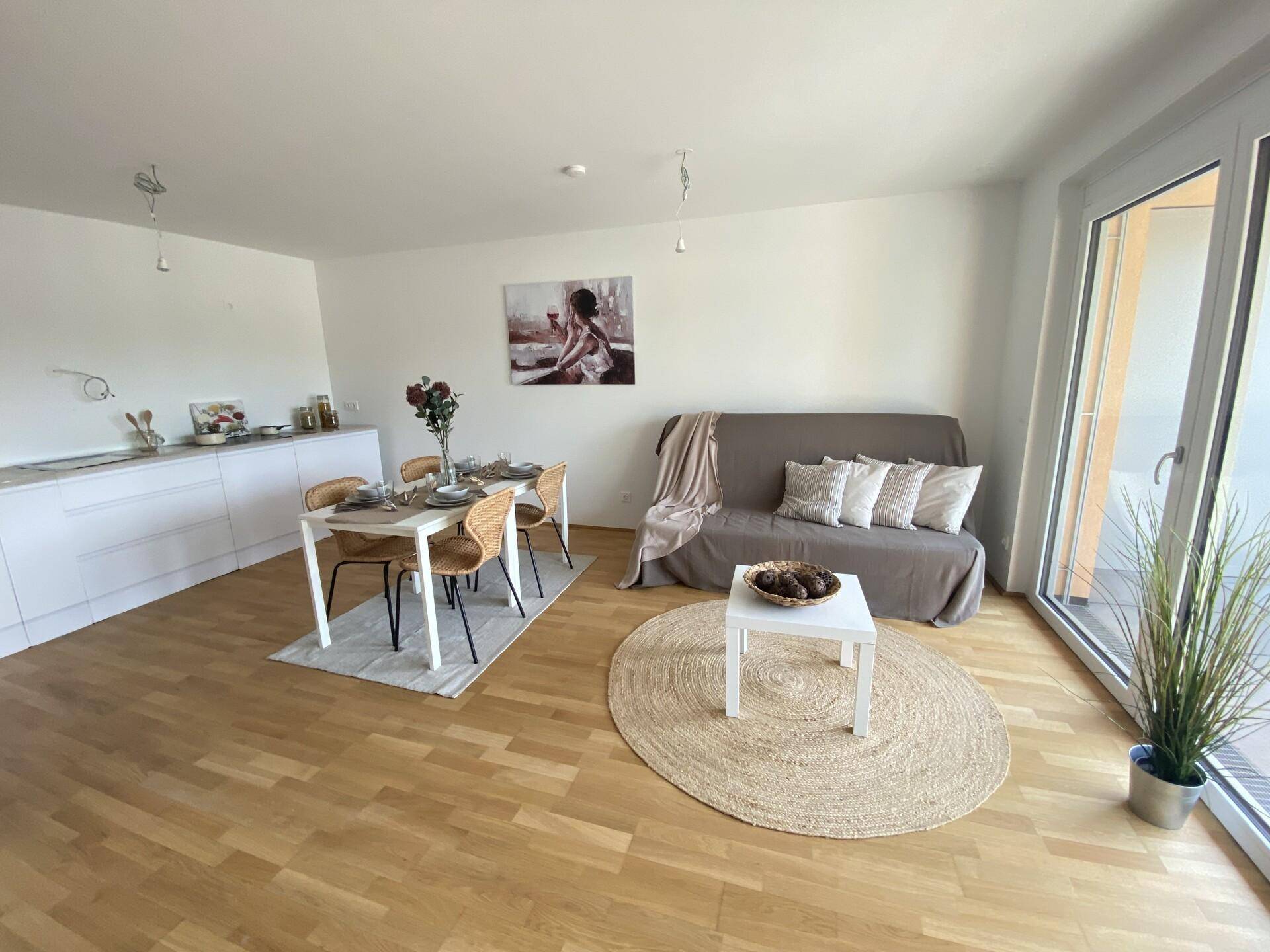Offener Wohn-Essbereich mit integrierter Küchenzeile, Holzboden und Zugang zum Balkon.