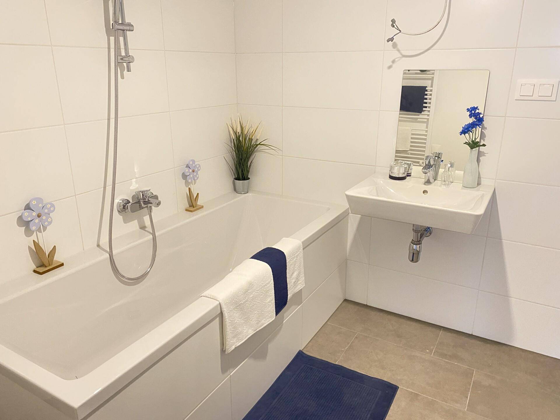 Modernes Badezimmer mit weiß gefliesten Wänden, Badewanne mit Duschfunktion und Einzelwaschbecken.