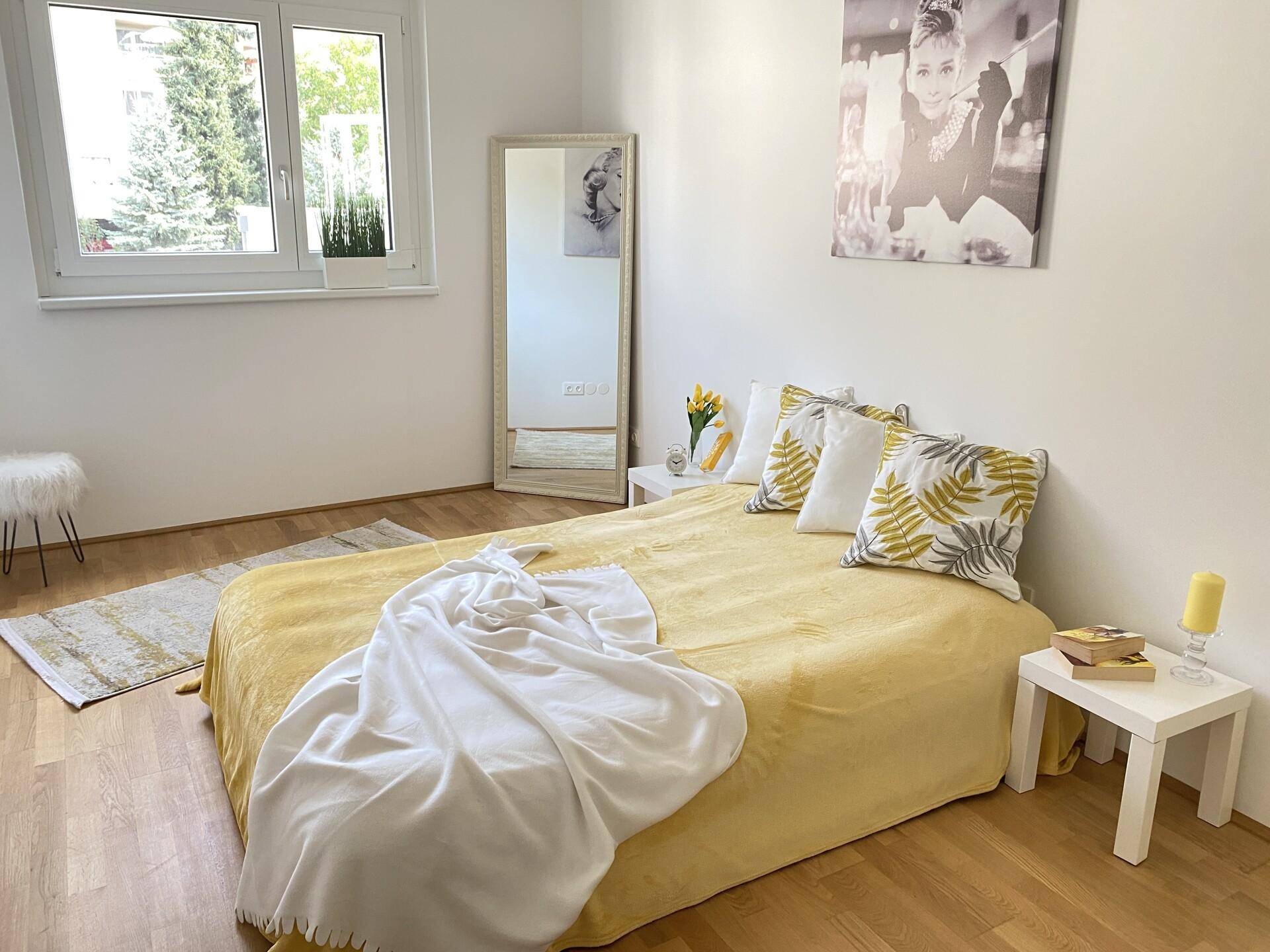 Helles Schlafzimmer mit Holzboden, großem Bett und einem Fenster mit Blick ins Grüne.