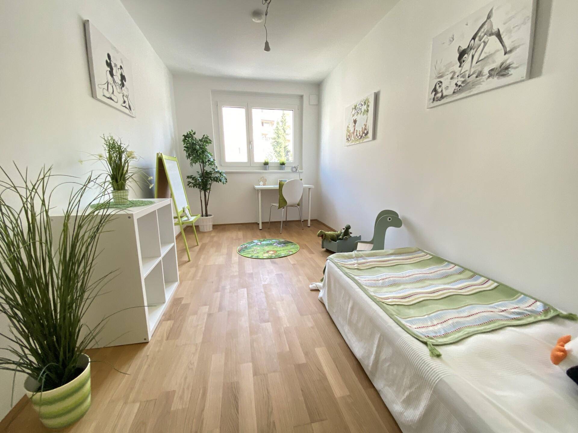 Kinderzimmer mit Holzboden, Einzelbett und einem Fenster, hell und freundlich eingerichtet.