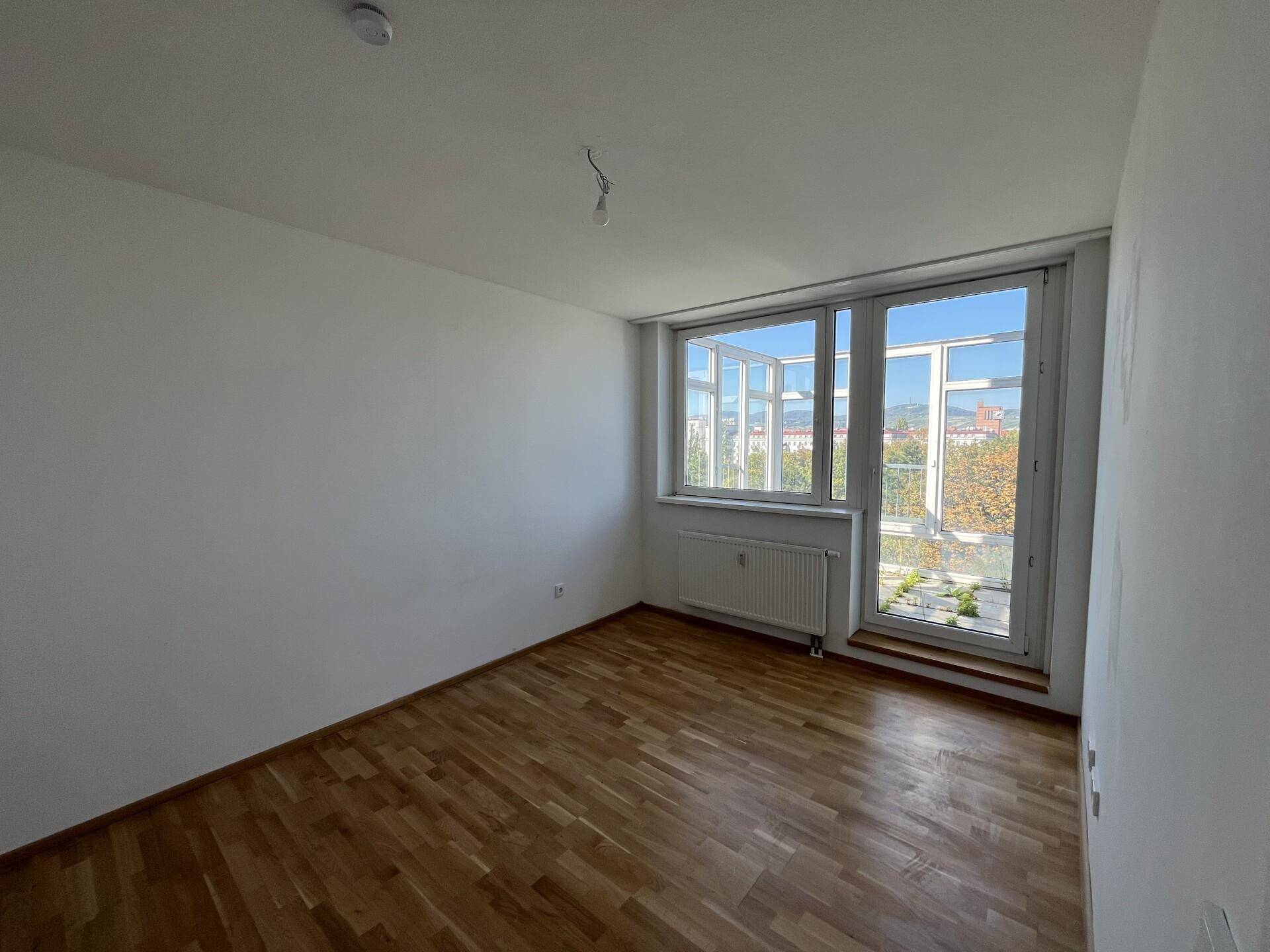 Helles Schlafzimmer mit Parkettboden, großen Fenstern und Zugang zum Außenbereich.