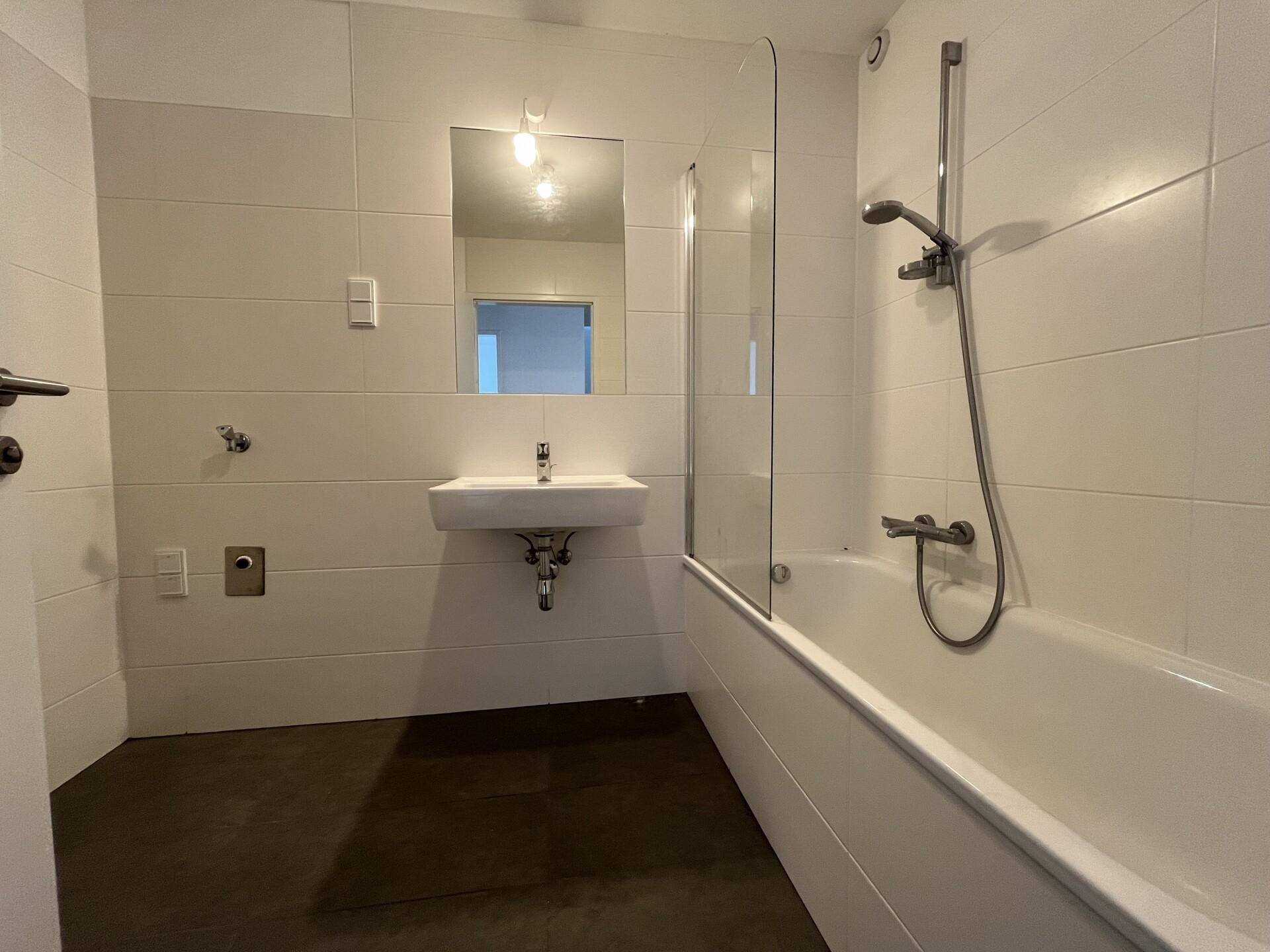 Helles Badezimmer mit Badewanne, Dusche, Einzelwaschbecken und weißen Fliesen.