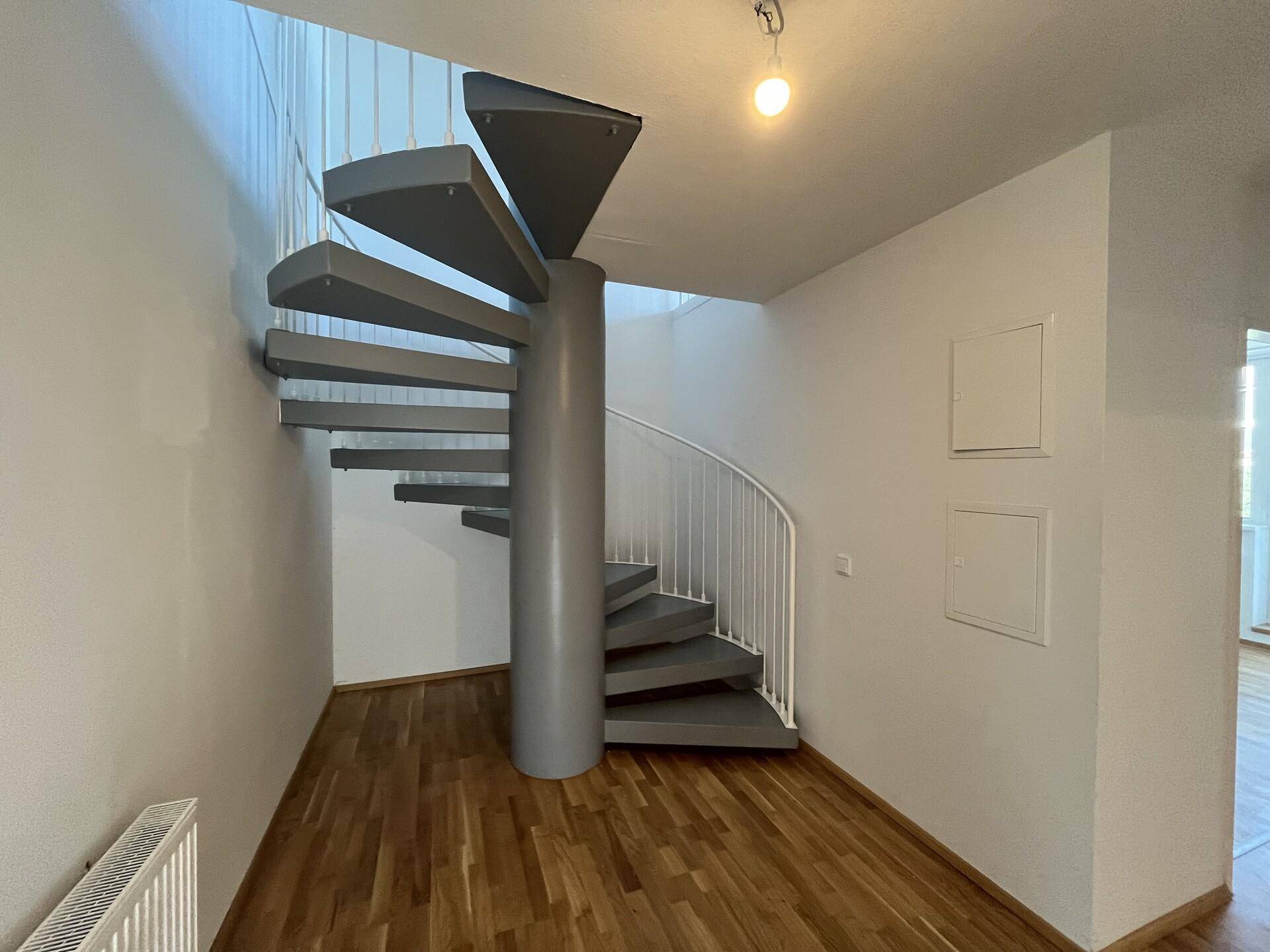 Heller Flur mit eleganter Wendeltreppe und Parkettboden.