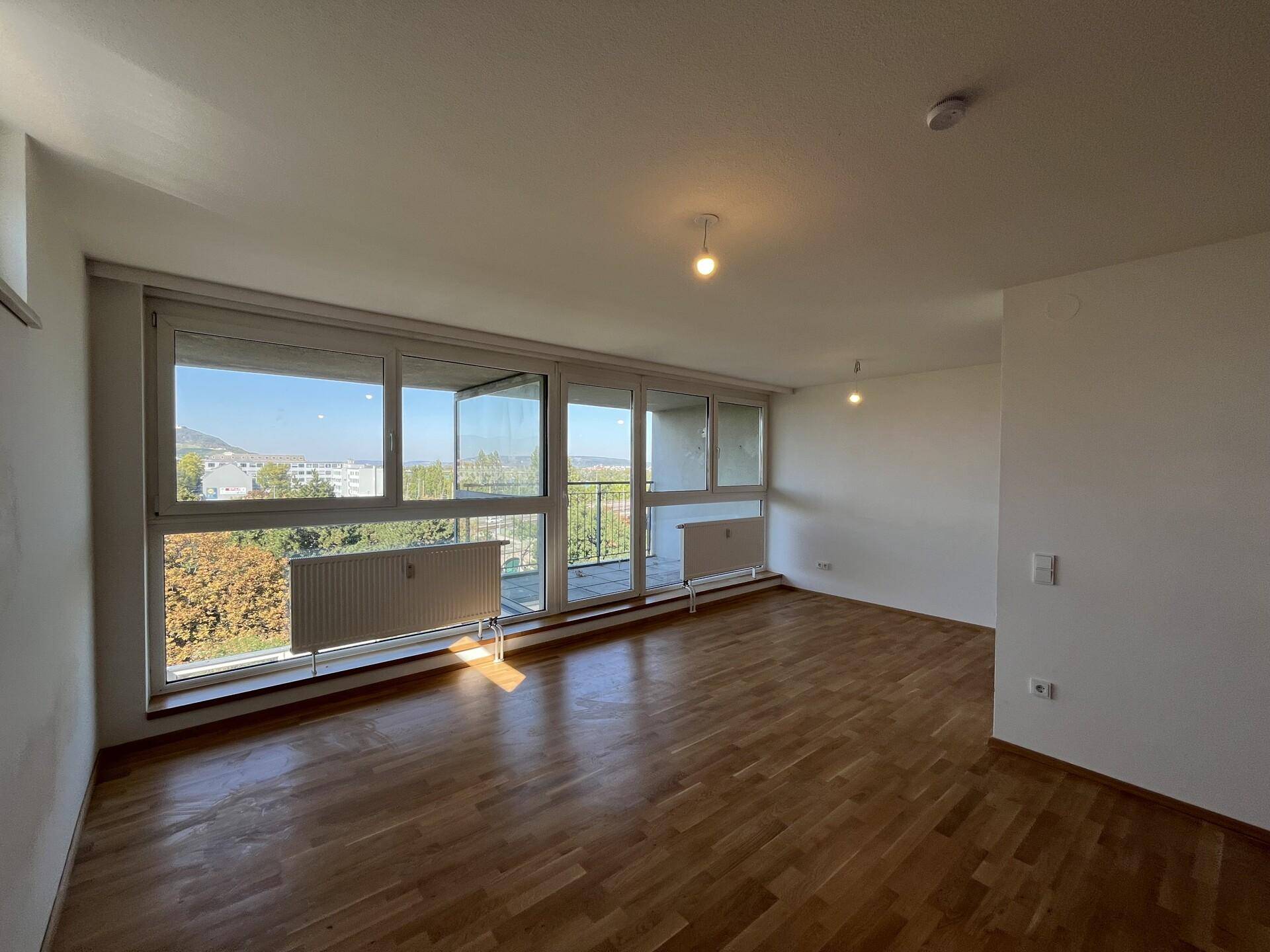 Helles Wohnzimmer mit Parkettboden, großen Fenstern und Blick ins Grüne.