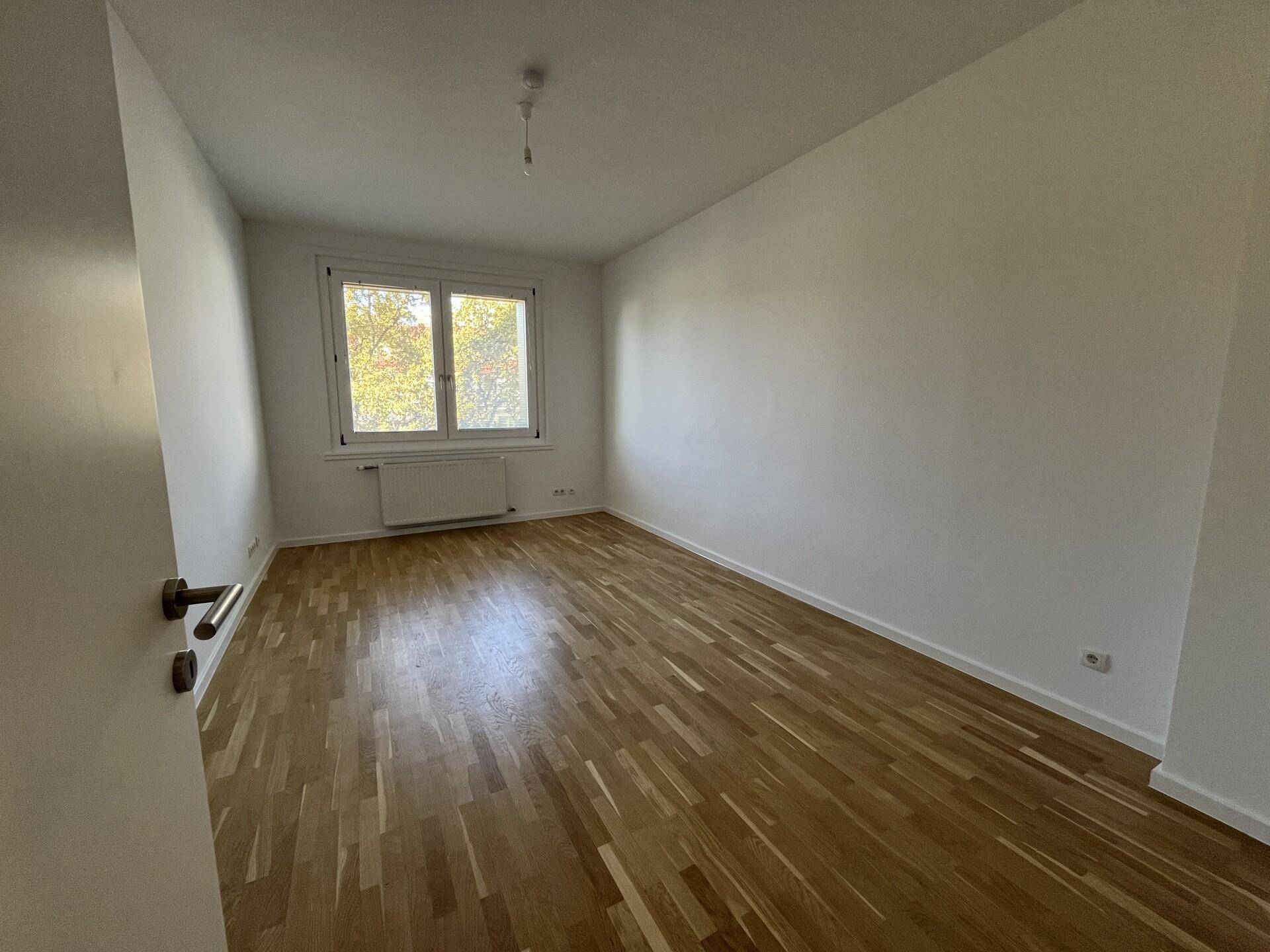 Helles Schlafzimmer mit Parkettboden und einem Fenster, das viel Tageslicht hereinlässt.