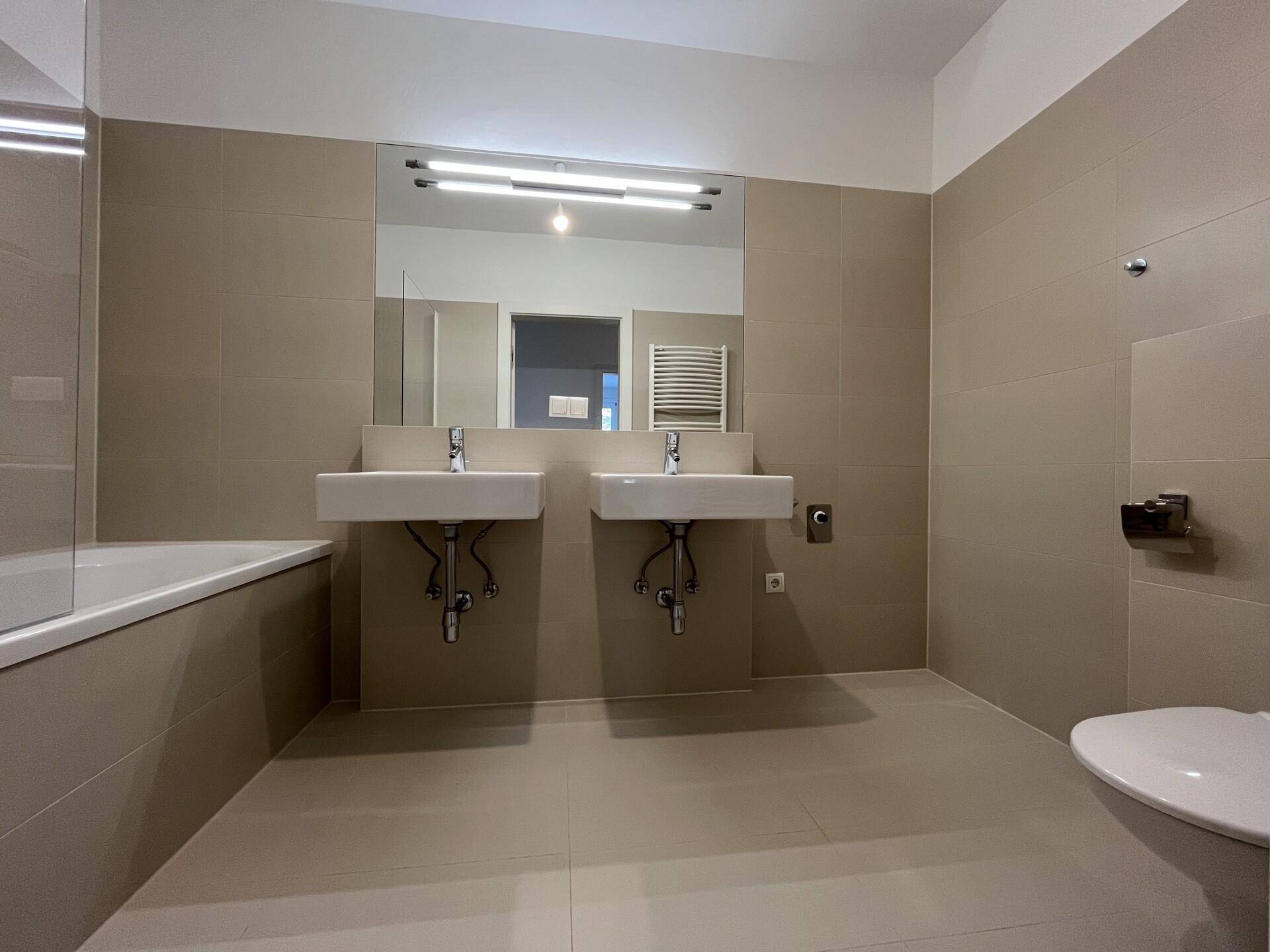 Modernes Badezimmer mit Doppelwaschbecken, Badewanne und beigefarbenen Fliesen.