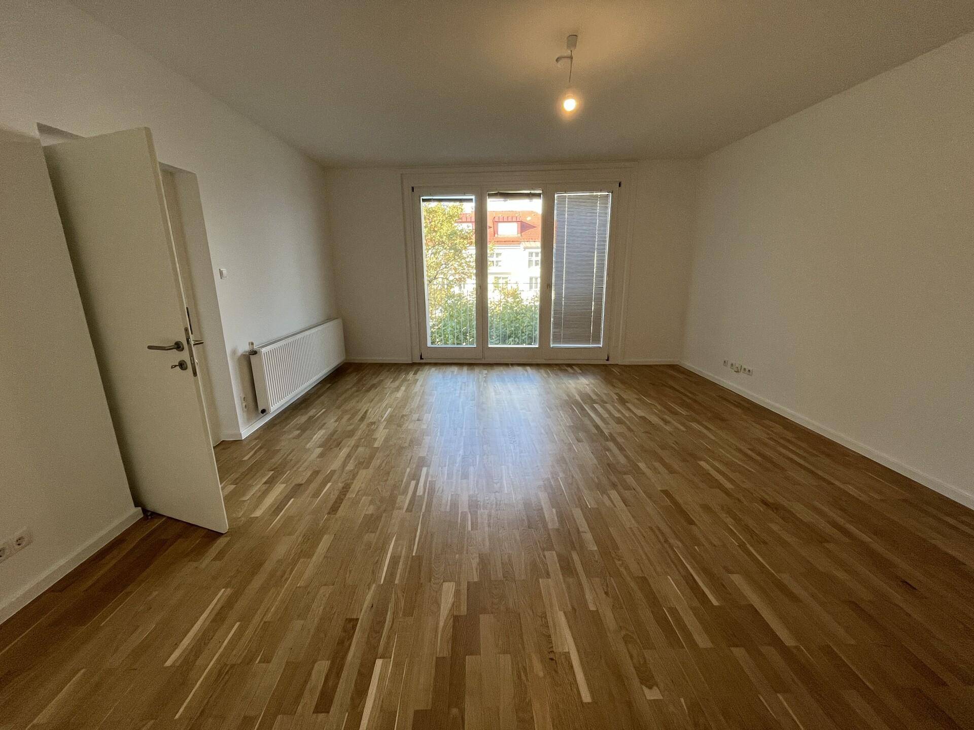 Geräumiger, heller Raum mit Parkettboden und großen Fenstertüren.