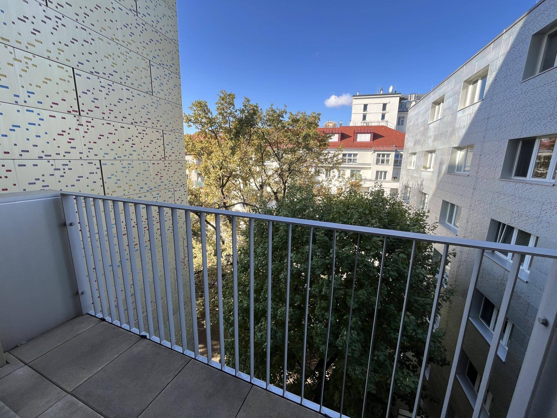 Kleiner Balkon mit Metallgeländer und Blick auf Bäume und umliegende Gebäude.