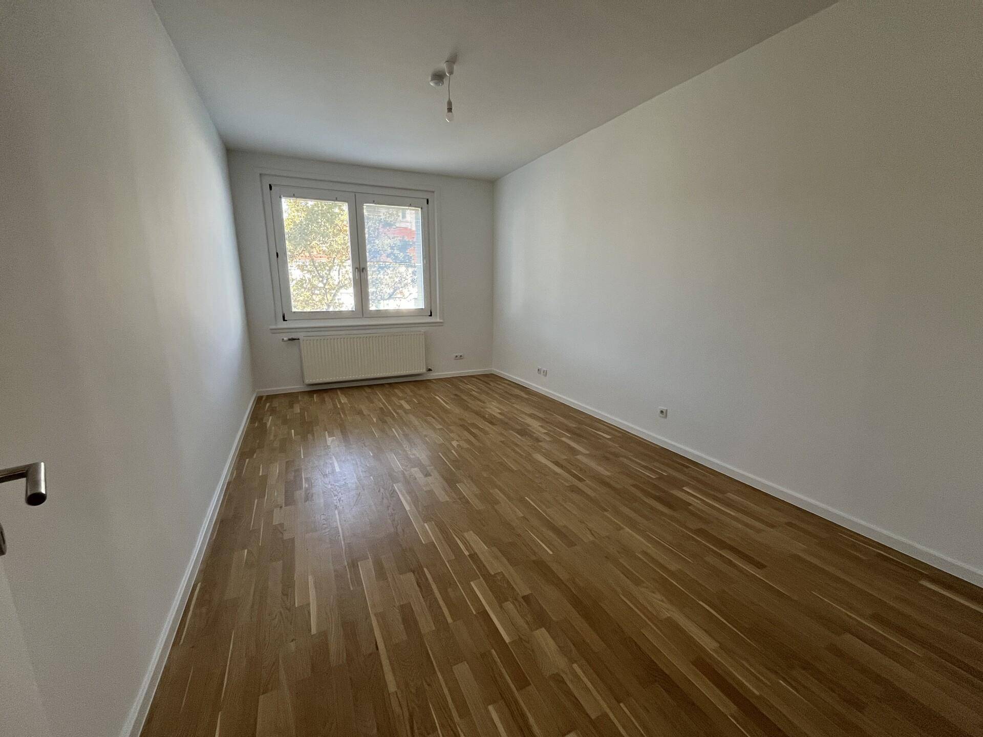 Geräumiges Schlafzimmer mit hellem Parkettboden und einem großen Fenster.