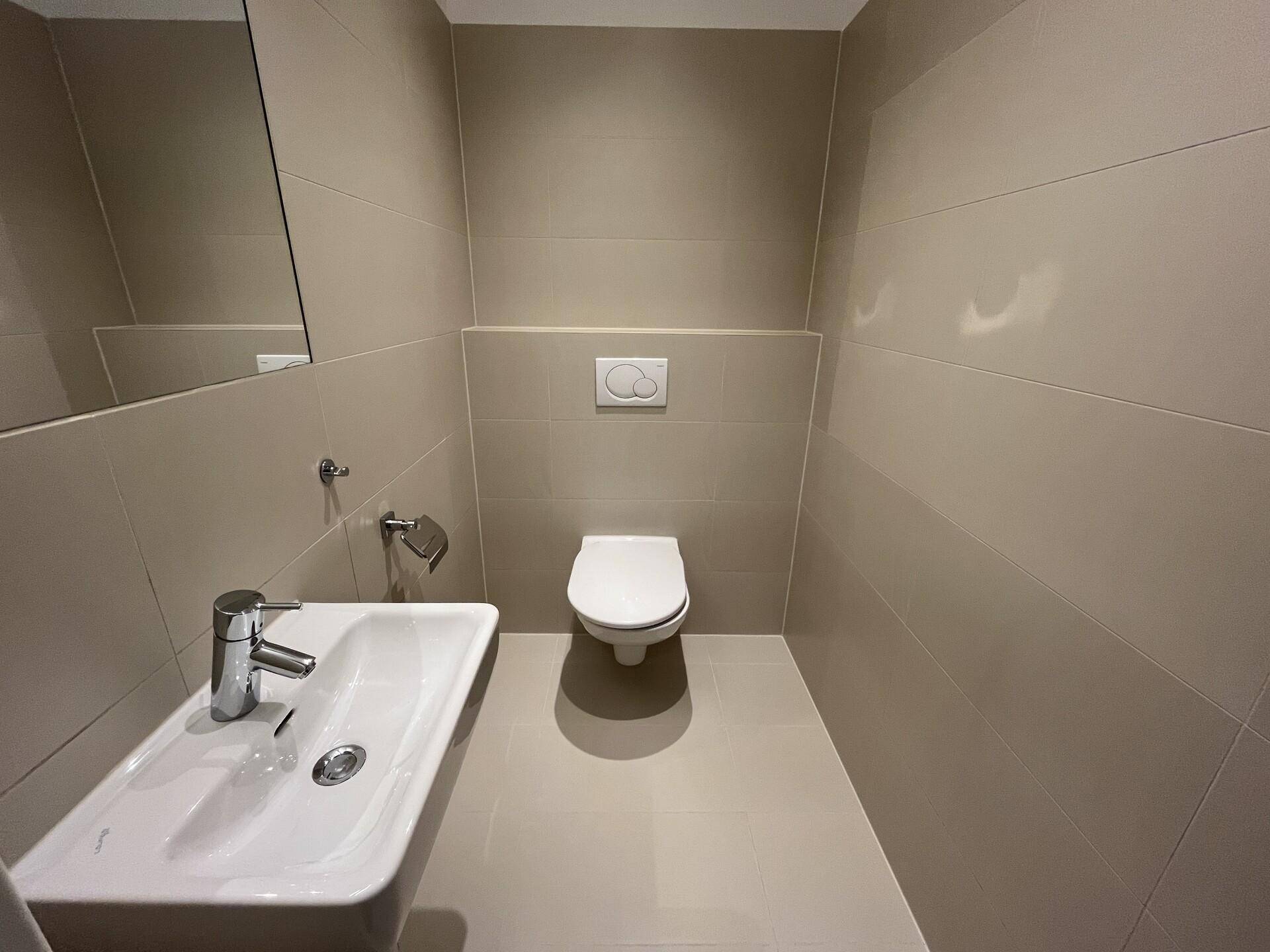 Modernes Gäste-WC mit Waschbecken, wandhängendem WC und beigefarbenen Fliesen.