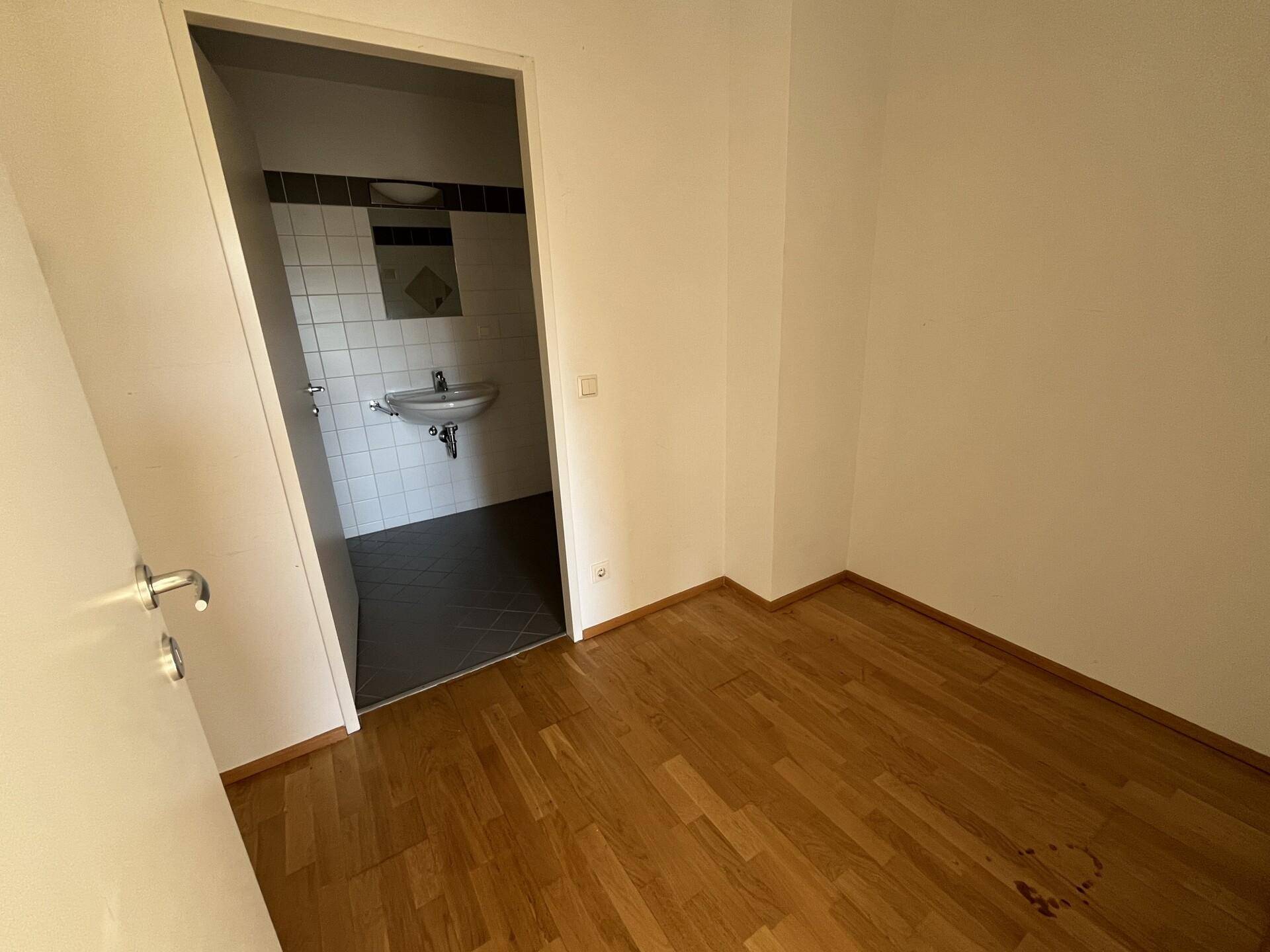 Kleiner Raum mit Parkettboden und direktem Zugang zu einem Badezimmer mit Waschbecken.