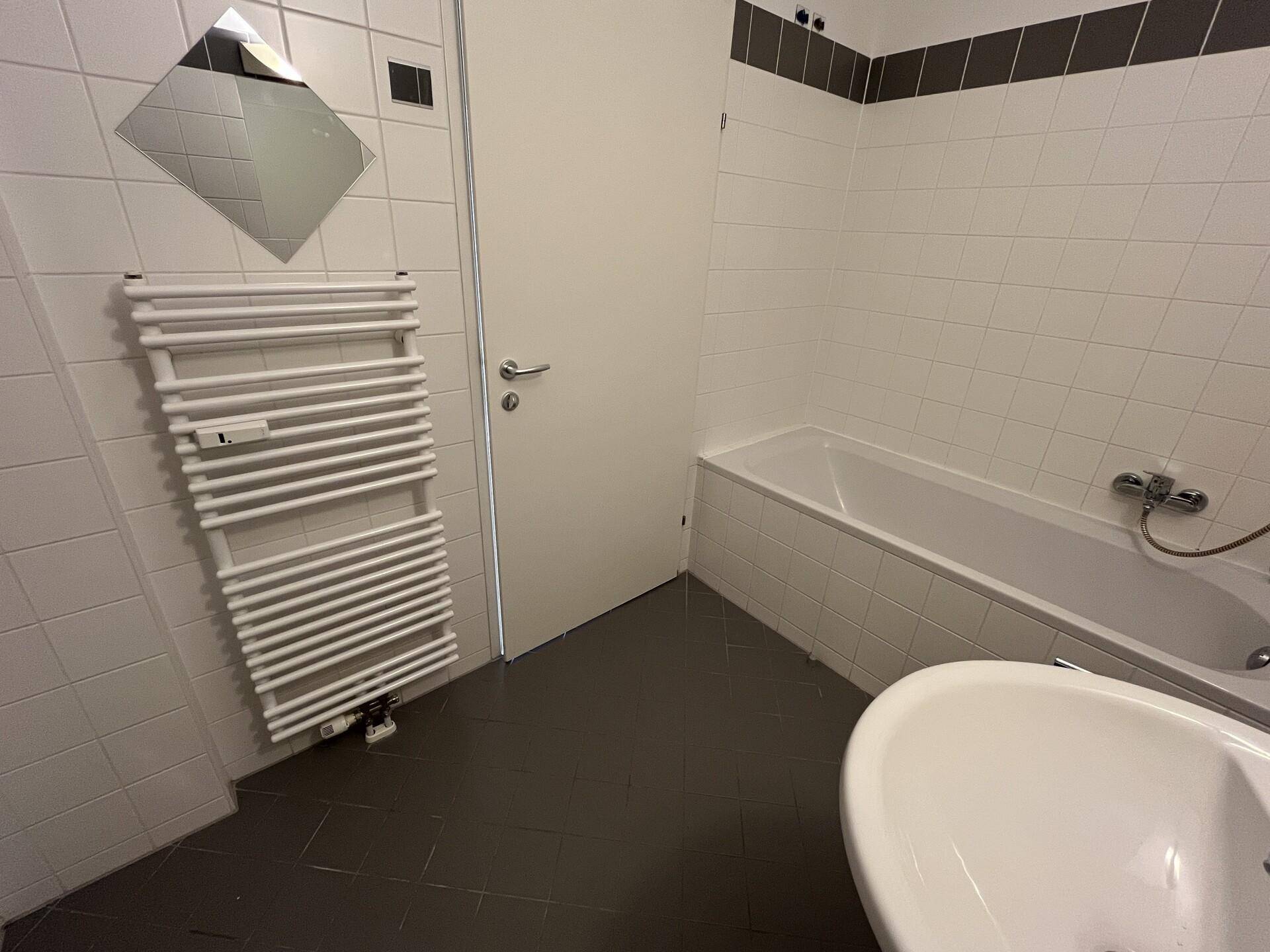 Badezimmer mit weißen Fliesen, einer Badewanne, einem Waschbecken und einem beheizten Handtuchhalter.