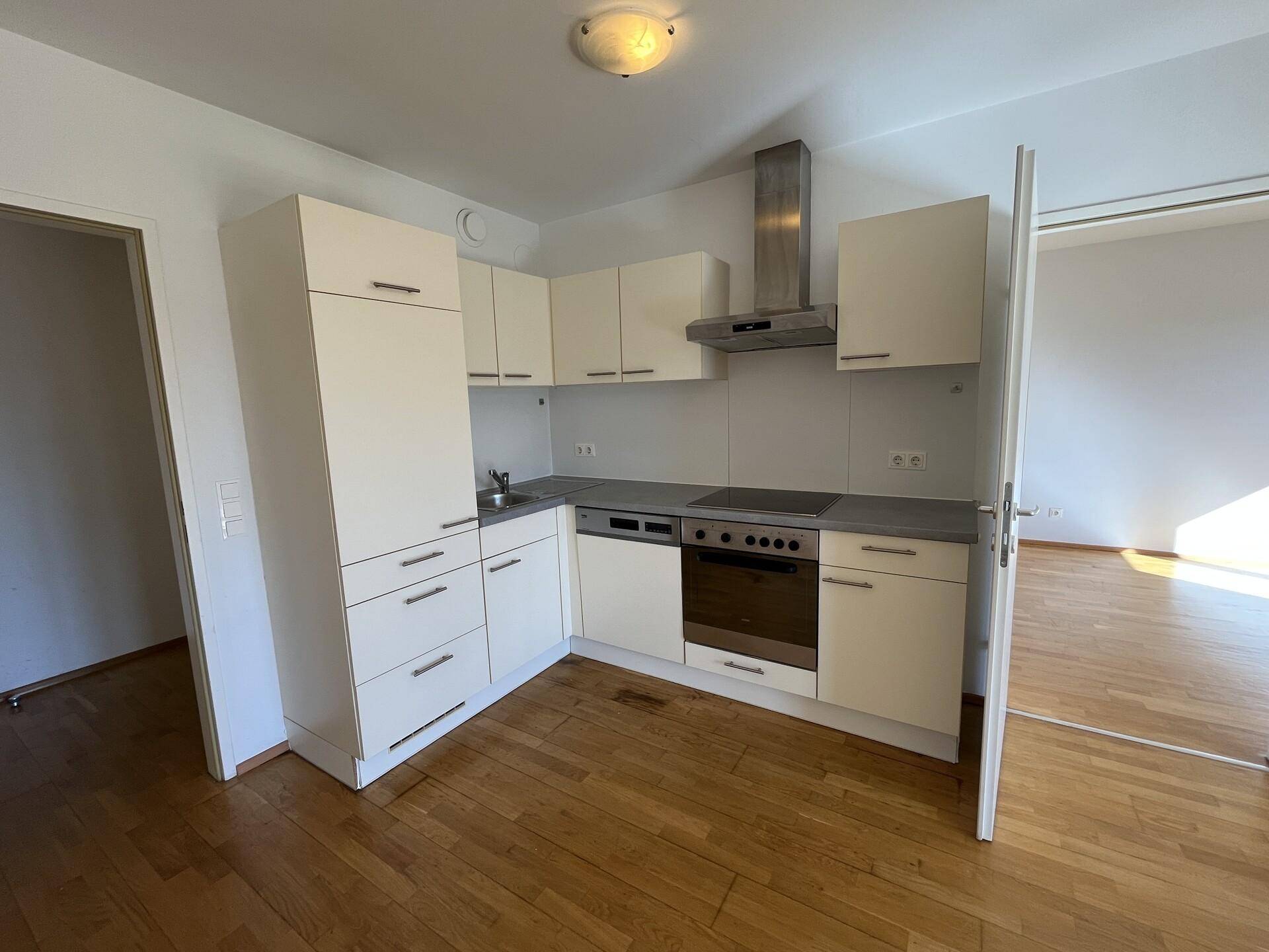 Funktionale Einbauküche mit hellen Schränken, Backofen, Kochfeld und Dunstabzugshaube.