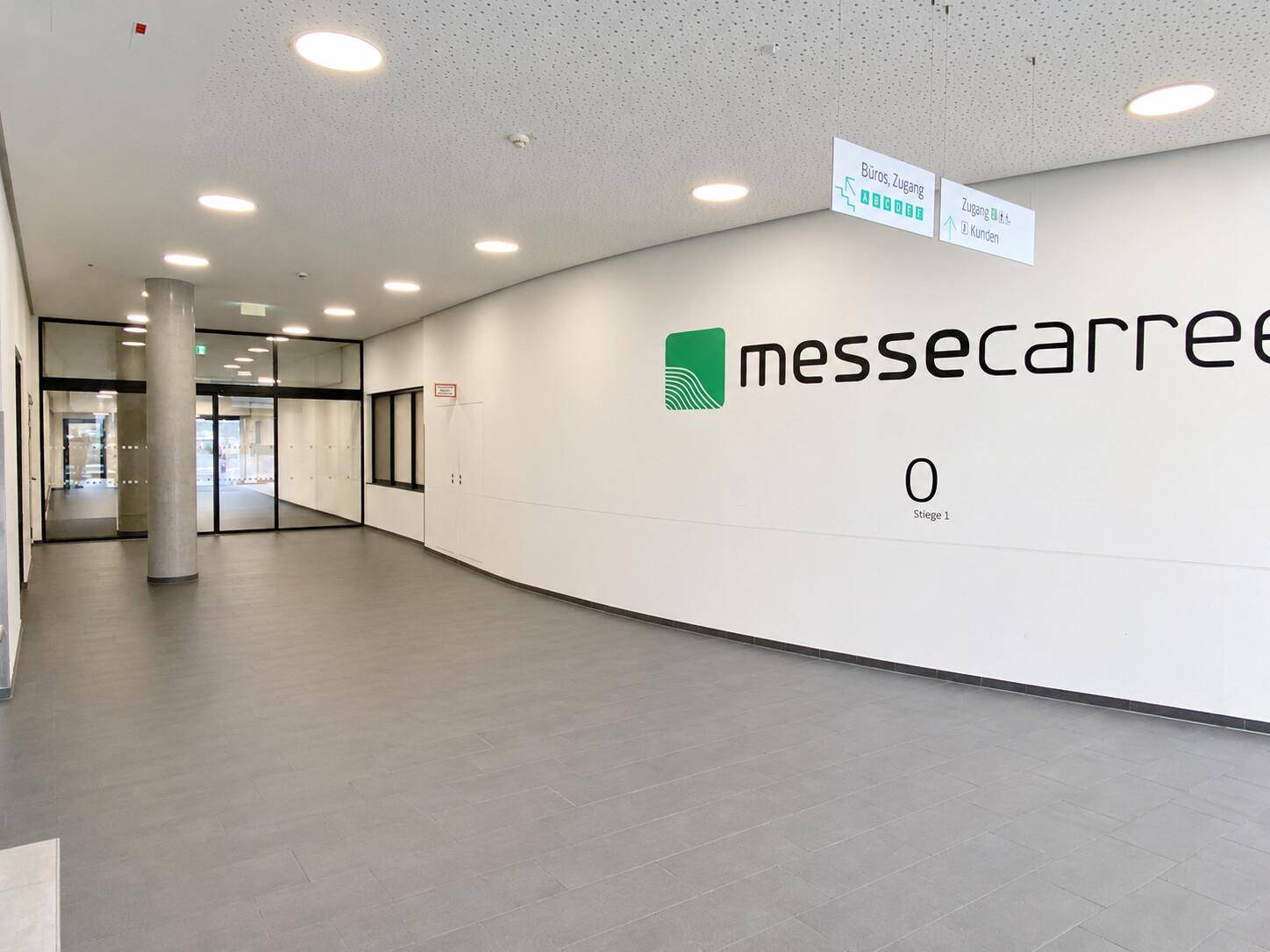 Heller Eingangsbereich mit großem Logo an der Wand, Fliesenboden und Wegweisern.