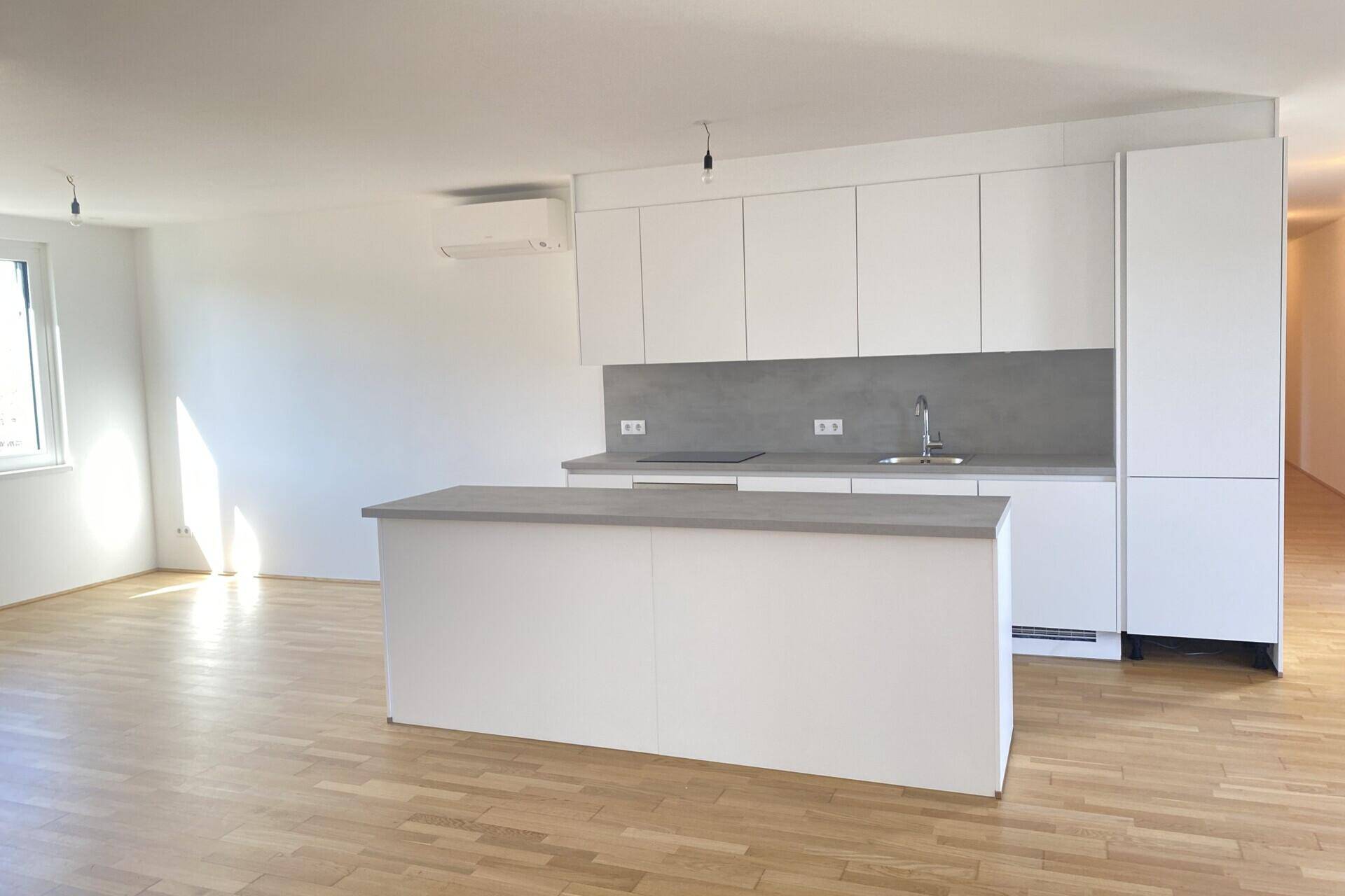 Moderne Einbauküche mit weißen Schränken, grauer Arbeitsplatte und integriertem Induktionskochfeld.