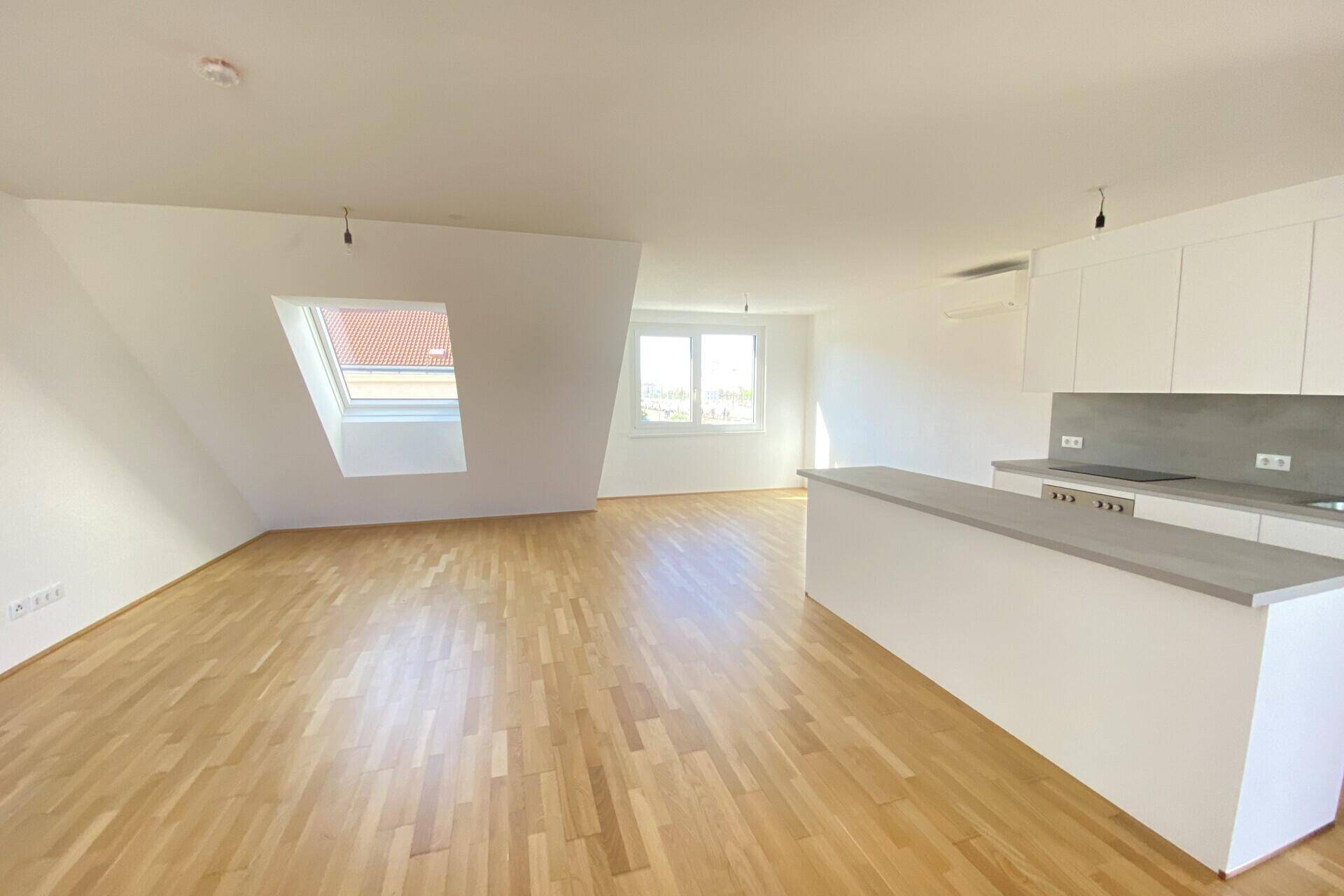 Lichtdurchfluteter Wohnbereich mit Dachschrägen, Parkettboden und integrierter Küchenzeile.