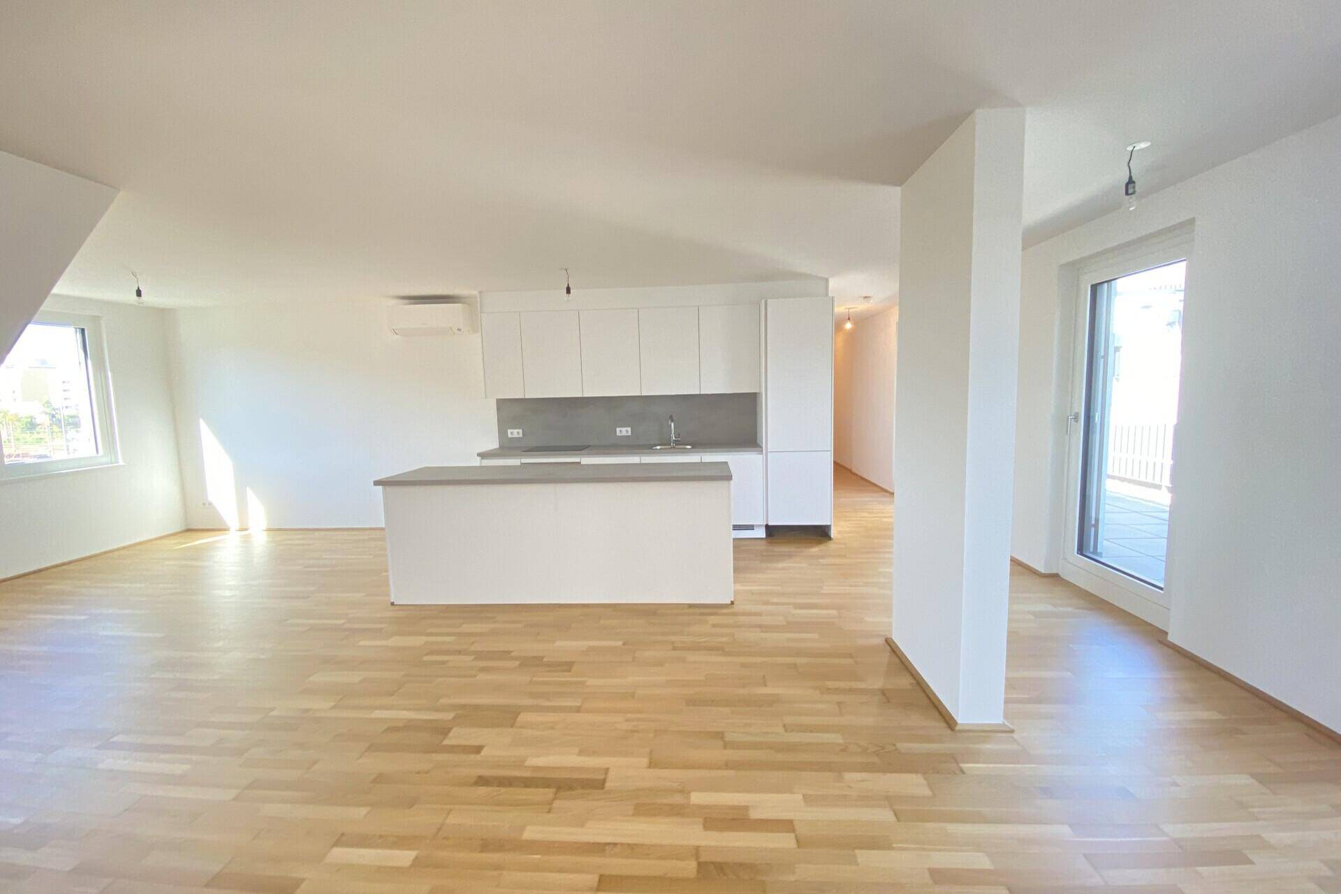 Heller offener Wohnbereich mit moderner Einbauküche, Kücheninsel und Zugang zur Terrasse.