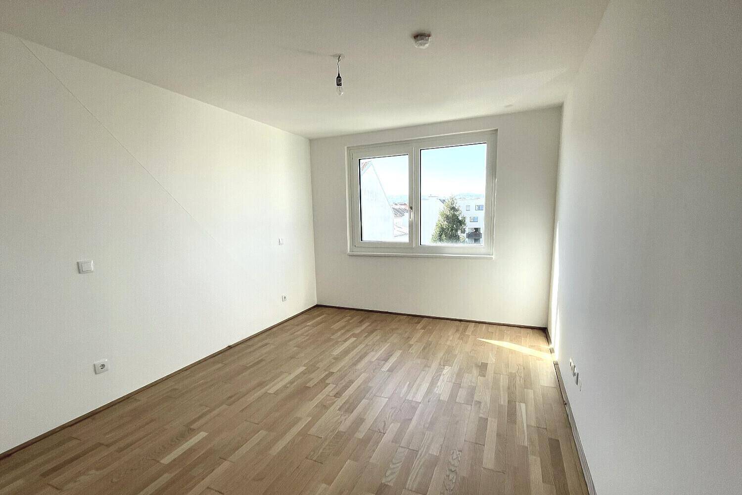 Geräumiges Zimmer mit hellem Parkettboden und einem großen Fenster für natürliche Belichtung.