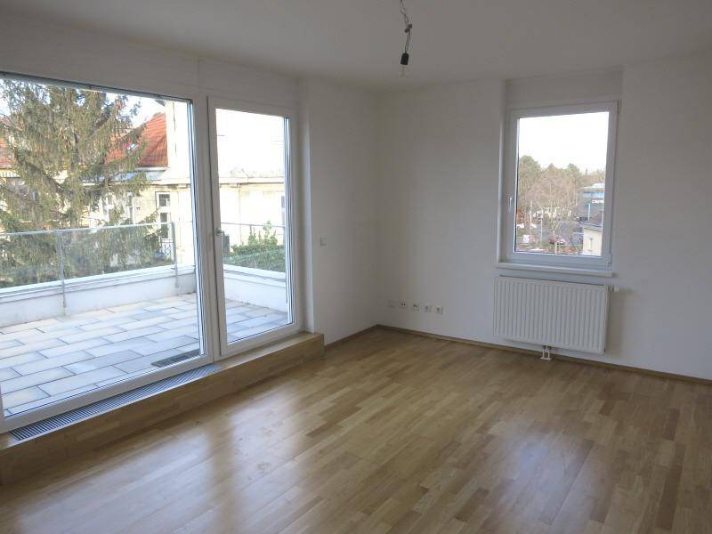 Heller Raum mit Holzboden, großen Fenstern und Zugang zu einer Terrasse.