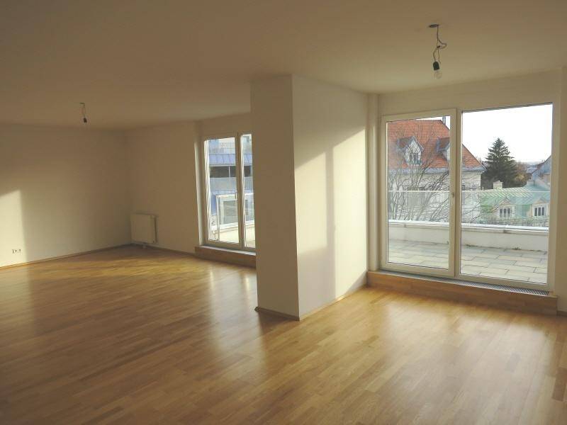 Heller, leerer Wohnbereich mit großen Fenstern und Zugang zur Terrasse.