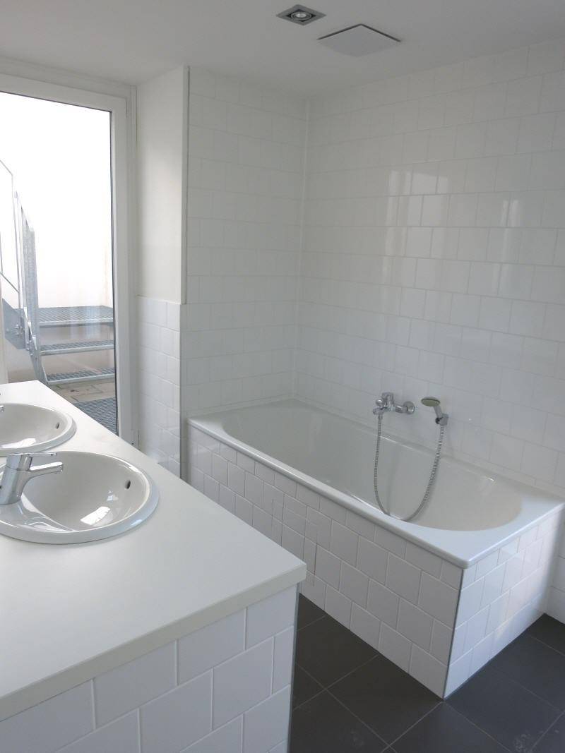 Helles Badezimmer mit Badewanne, Doppelwaschbecken und weißen Fliesen.