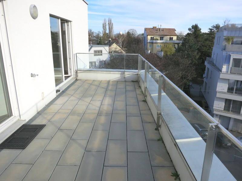 Sonniger Terrassenbereich mit Glasgeländer und Blick auf umliegende Gebäude.