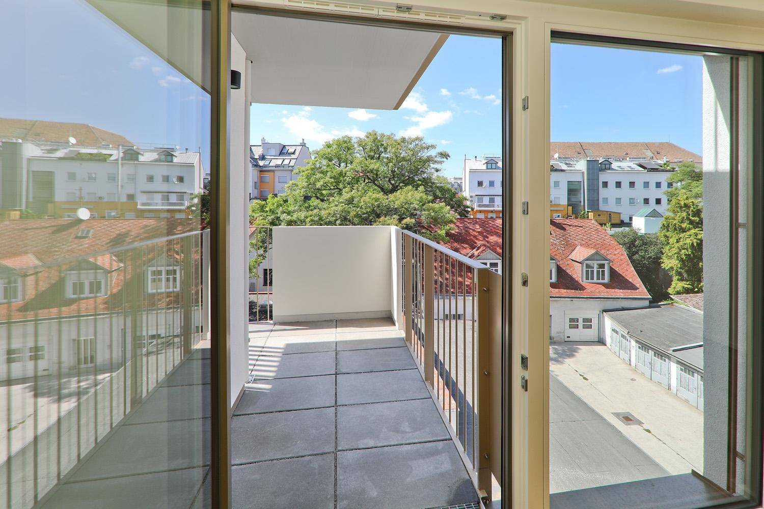 Heller Balkon mit Fliesenboden und Metallgeländer, zugänglich durch eine große Glasschiebetür.