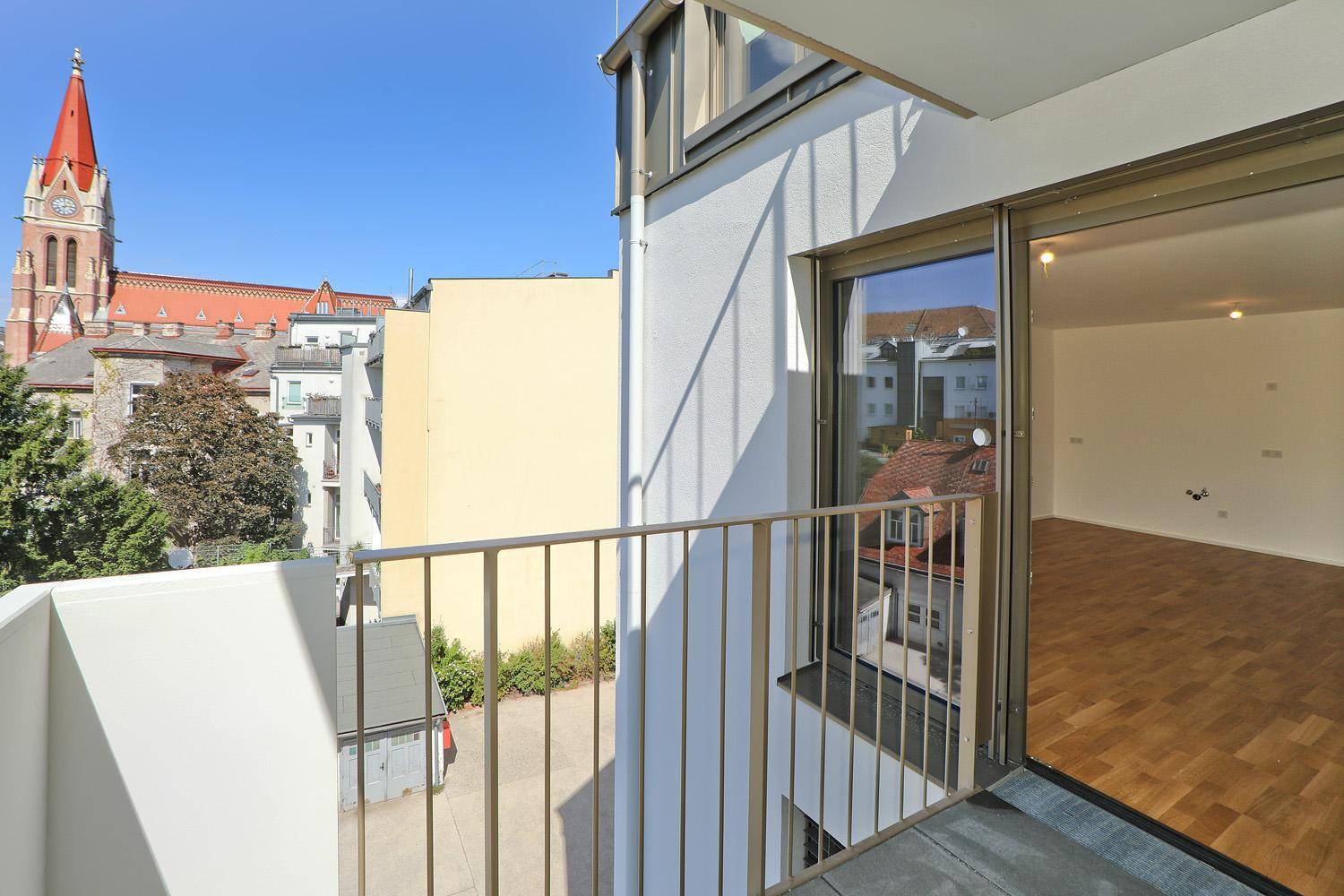 Balkon mit Blick auf die moderne Gebäudefassade und die umliegende Stadt mit einer Kirche.