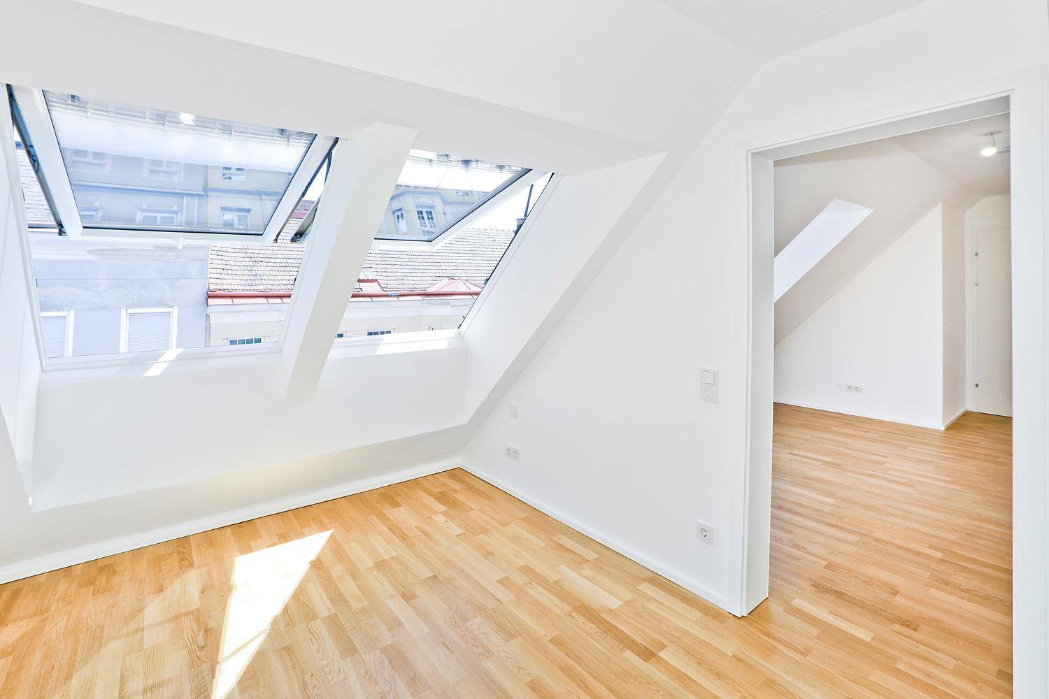 Heller Raum im Dachgeschoss mit Holzparkettboden, weißen Wänden und großen Dachfenstern.