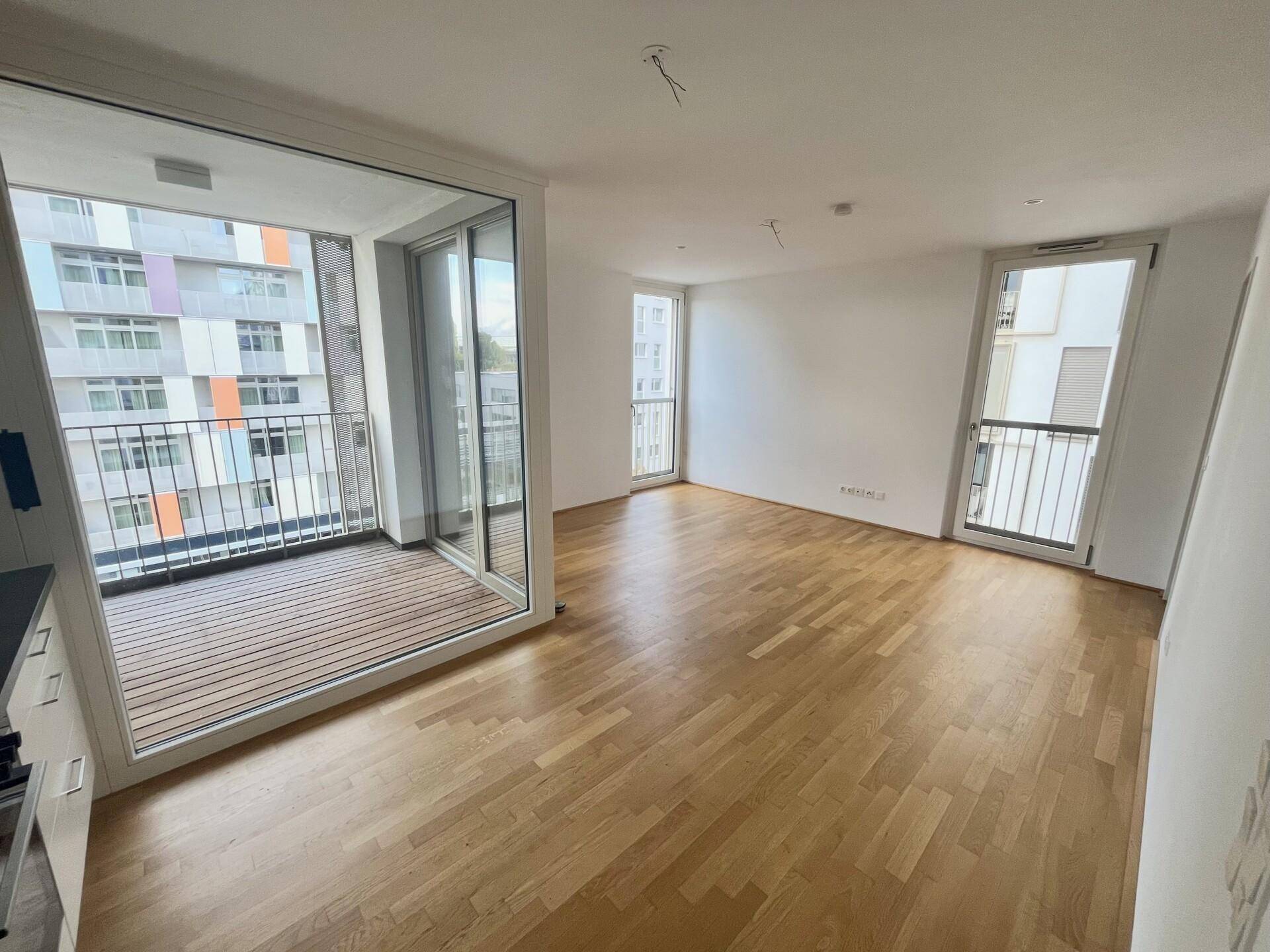 Heller Wohnbereich mit Parkettboden und großen Fensterfronten, die viel Tageslicht hereinlassen.
