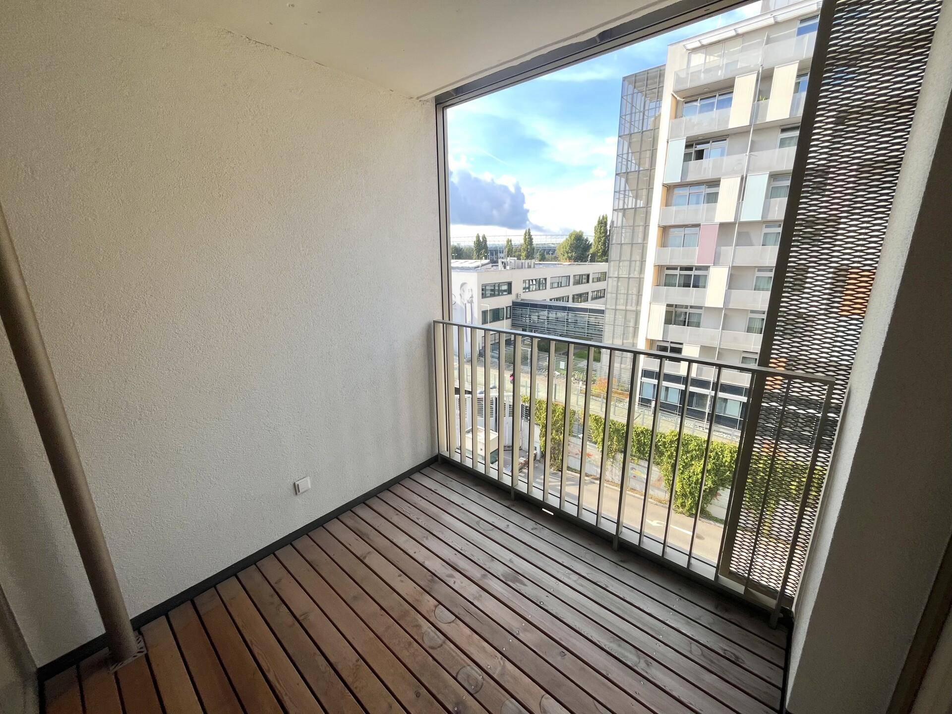 Kleiner Balkon mit Holzfußboden und Blick auf moderne Wohngebäude in der Umgebung.