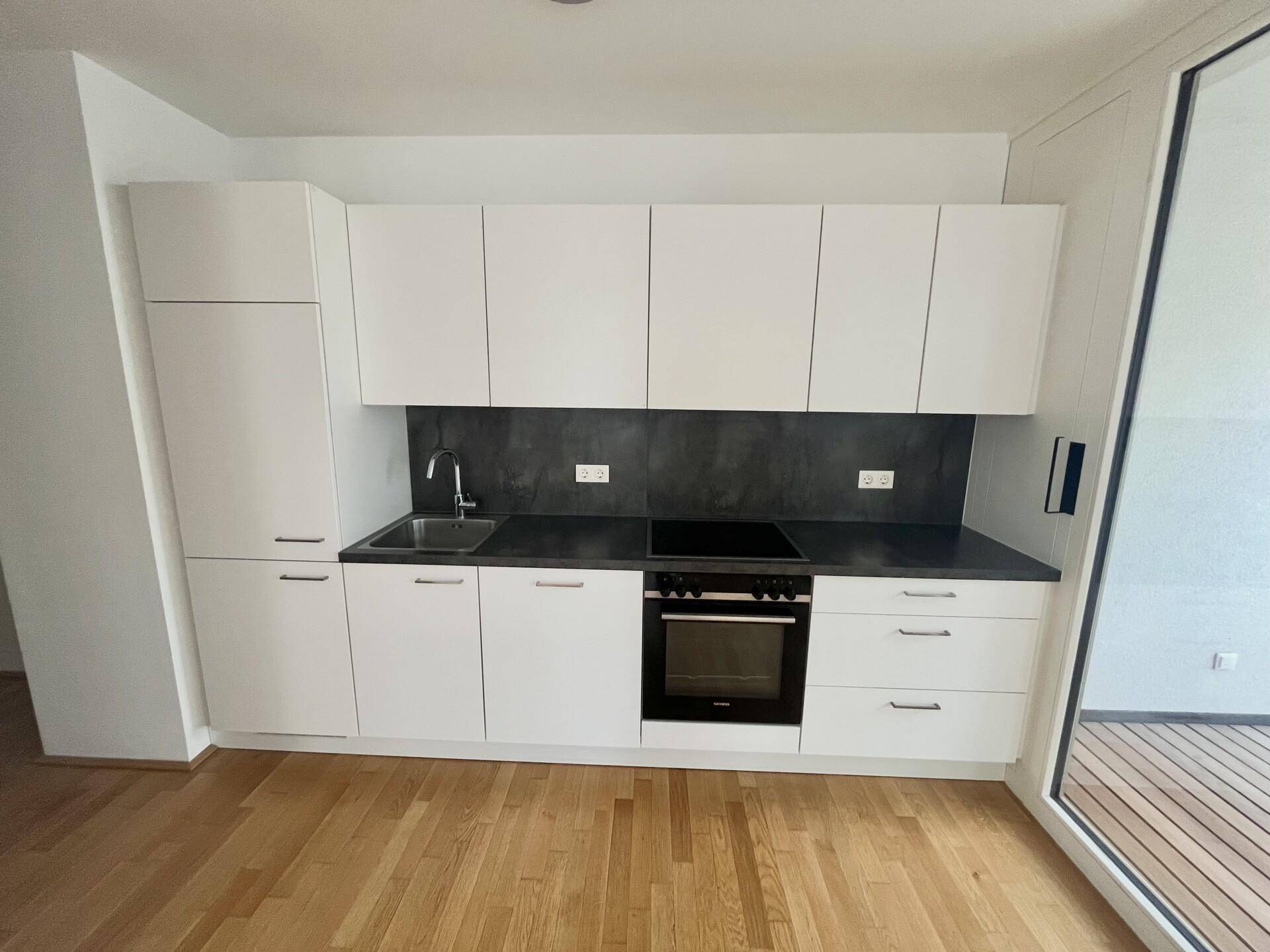 Moderne Einbauküche mit weißen Schränken, dunkler Arbeitsplatte und integrierten Geräten.