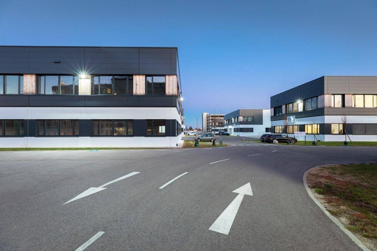 Ansicht eines modernen Gewerbeparks bei Dämmerung mit beleuchteten Gebäuden und Zufahrtsstraßen.