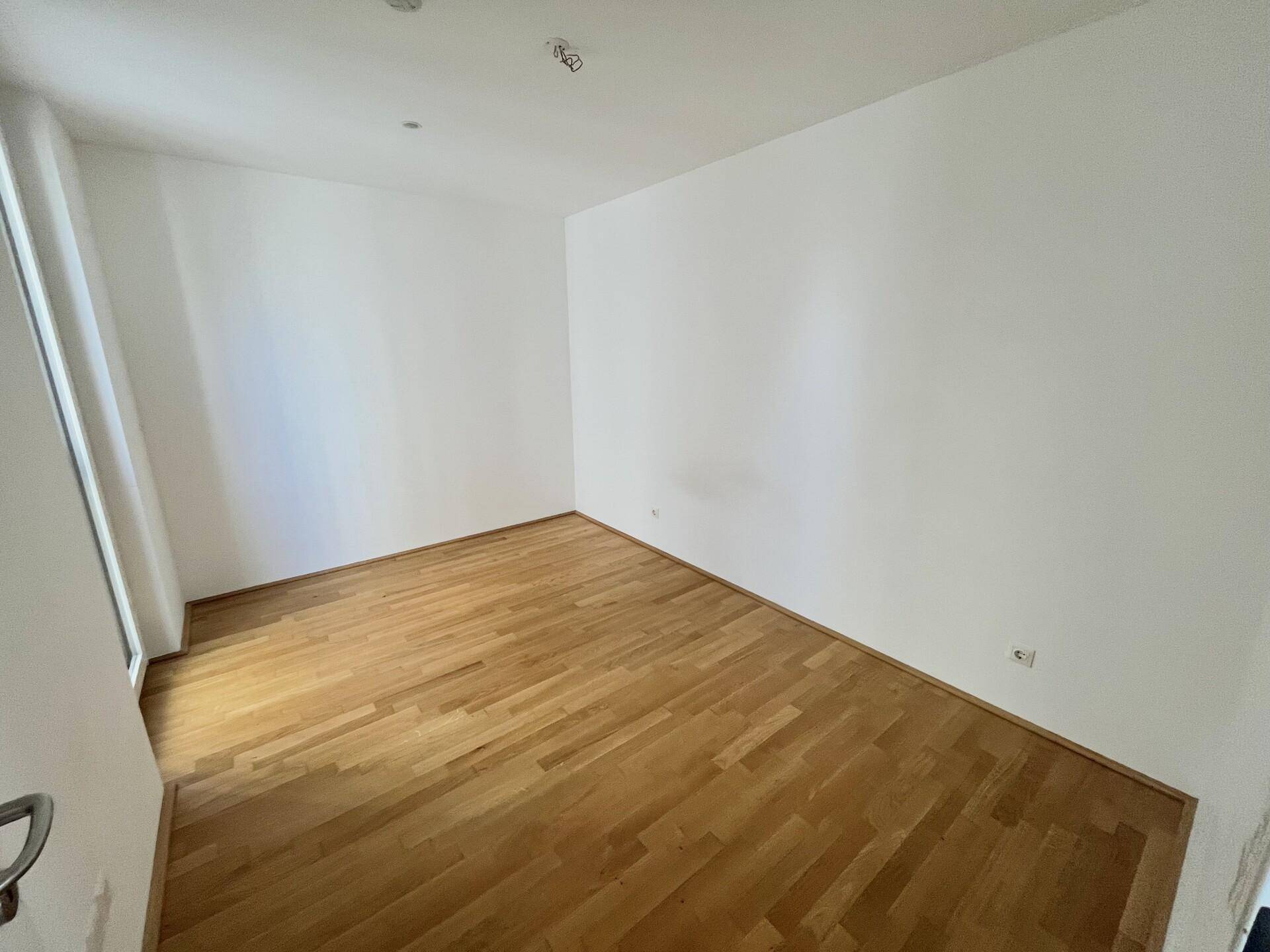 Heller Raum mit weißen Wänden und Parkettboden, ideal als Wohn- oder Schlafzimmer.