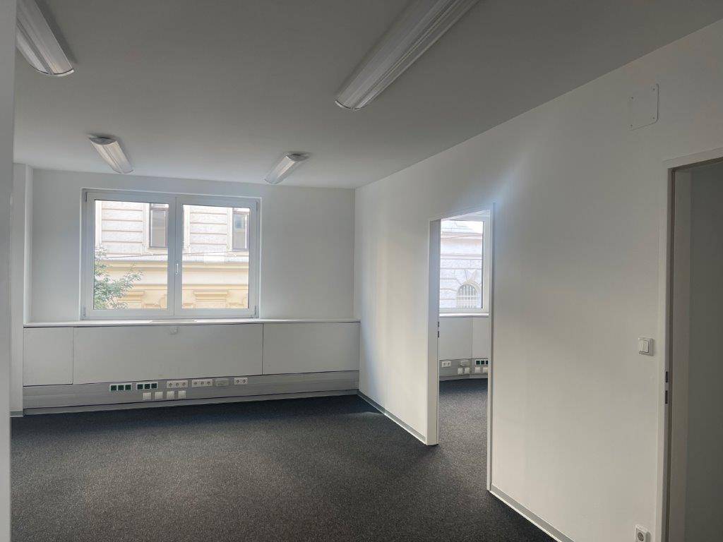 Geräumiges Büro mit Teppichboden, großen Fenstern und einem Durchgang zu einem weiteren Raum.