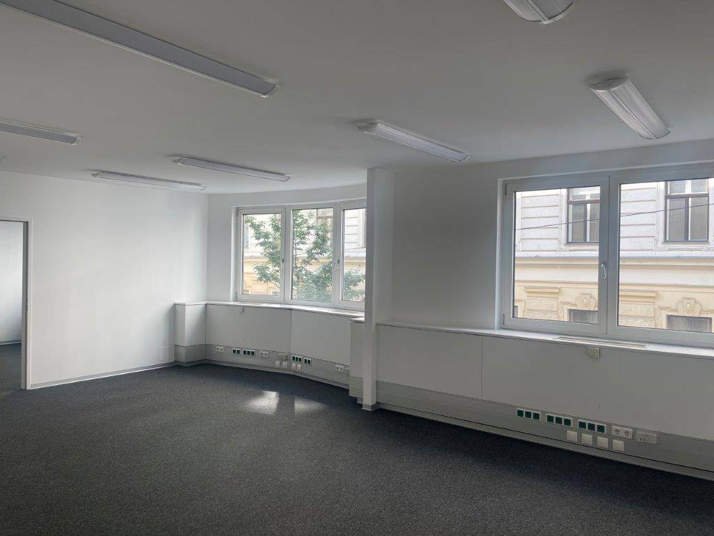 Helles Büro mit Teppichboden, gebogener Wand und mehreren Fenstern mit Blick auf die Umgebung.