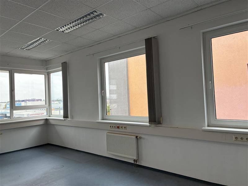 Heller Büroraum mit mehreren Fenstern, die einen Blick auf die Umgebung und andere Gebäude bieten, mit Standardausstattung.