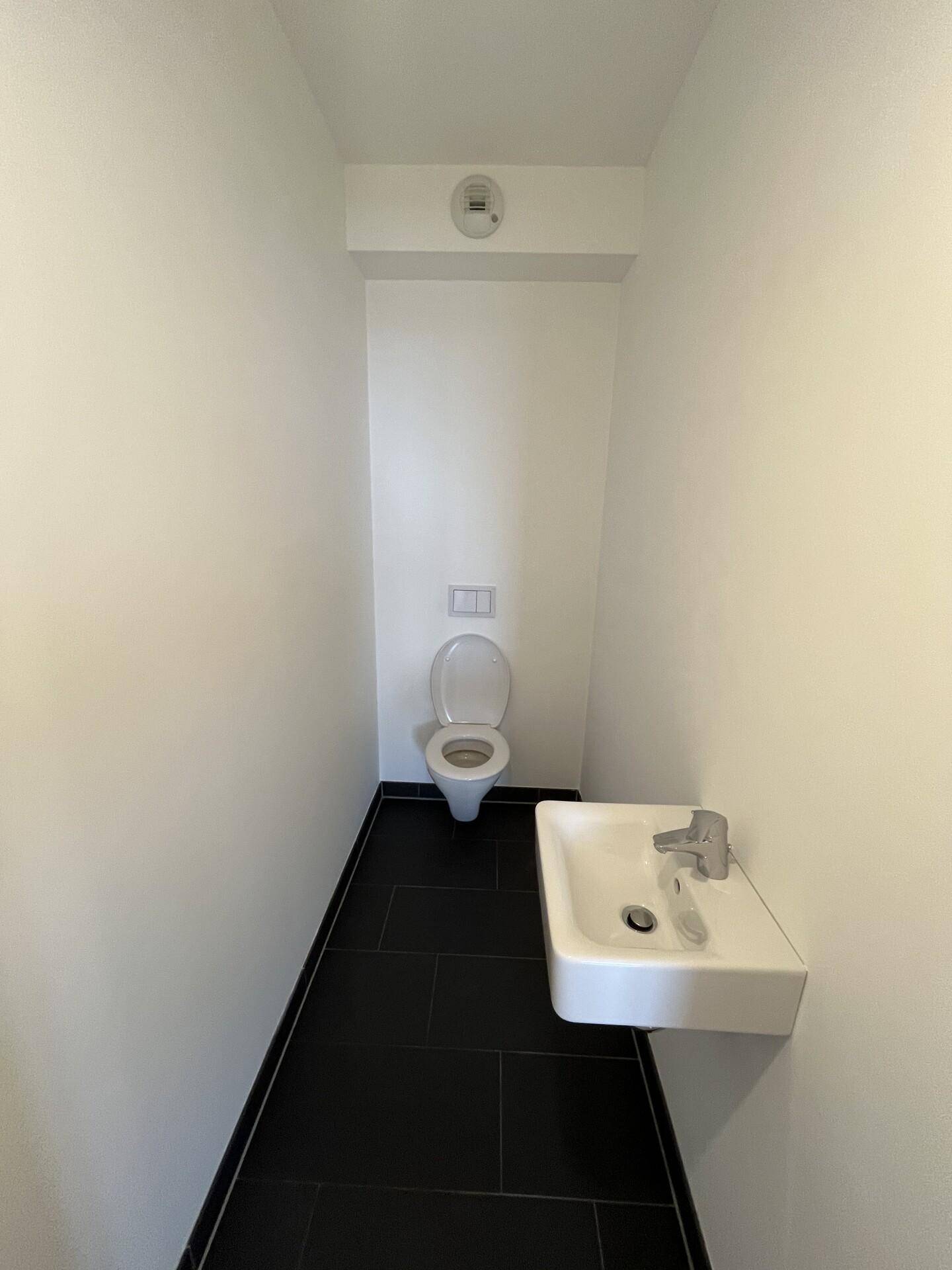 Separates Gäste-WC mit Wand-WC, kleinem Waschbecken und dunklen Bodenfliesen.