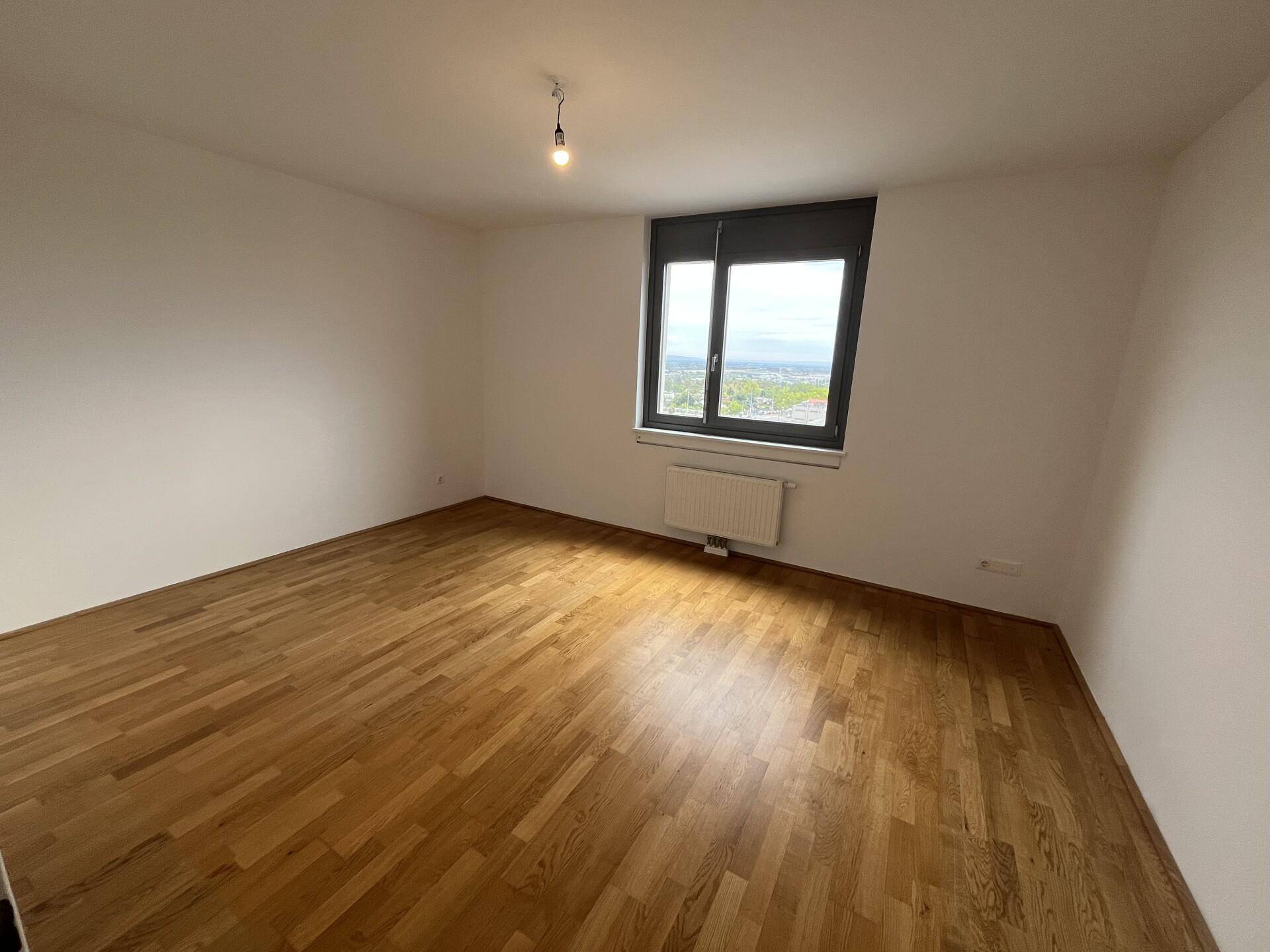 Leeres Schlafzimmer mit Holzparkettboden und einem Fenster, das viel Tageslicht hereinlässt.